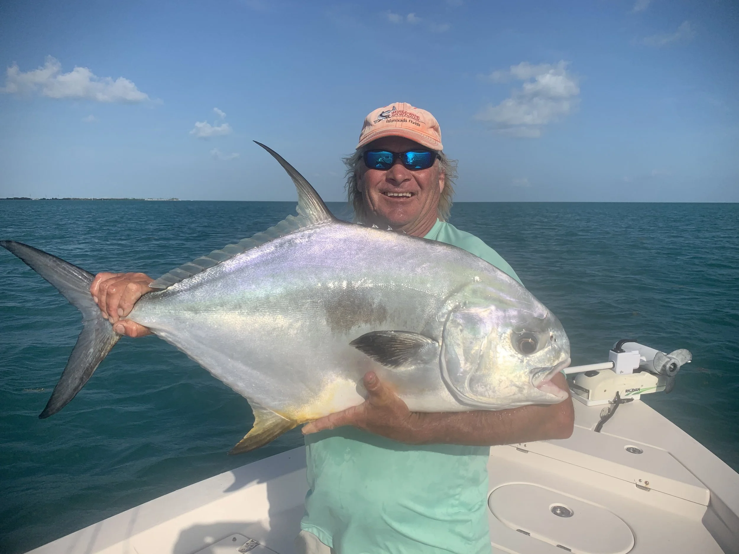 A man on a boat holding a large fish he caught, with the ocean and sky in the background.