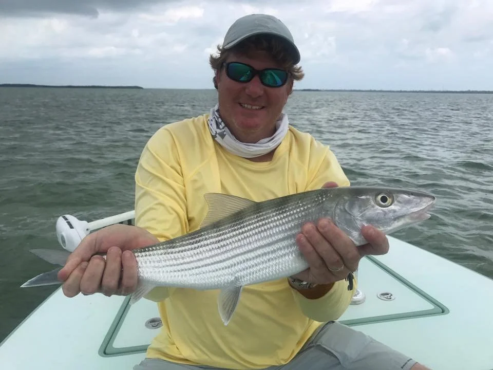 Man in yellow shirt on boat holding a striped fish over water.