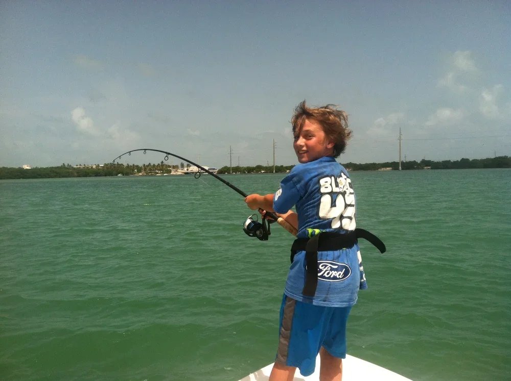 Boy fishing on a boat in a body of water.