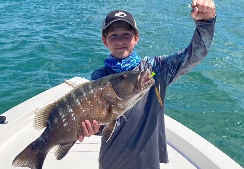 A young boy on a boat holding a large fish he just caught in the water.