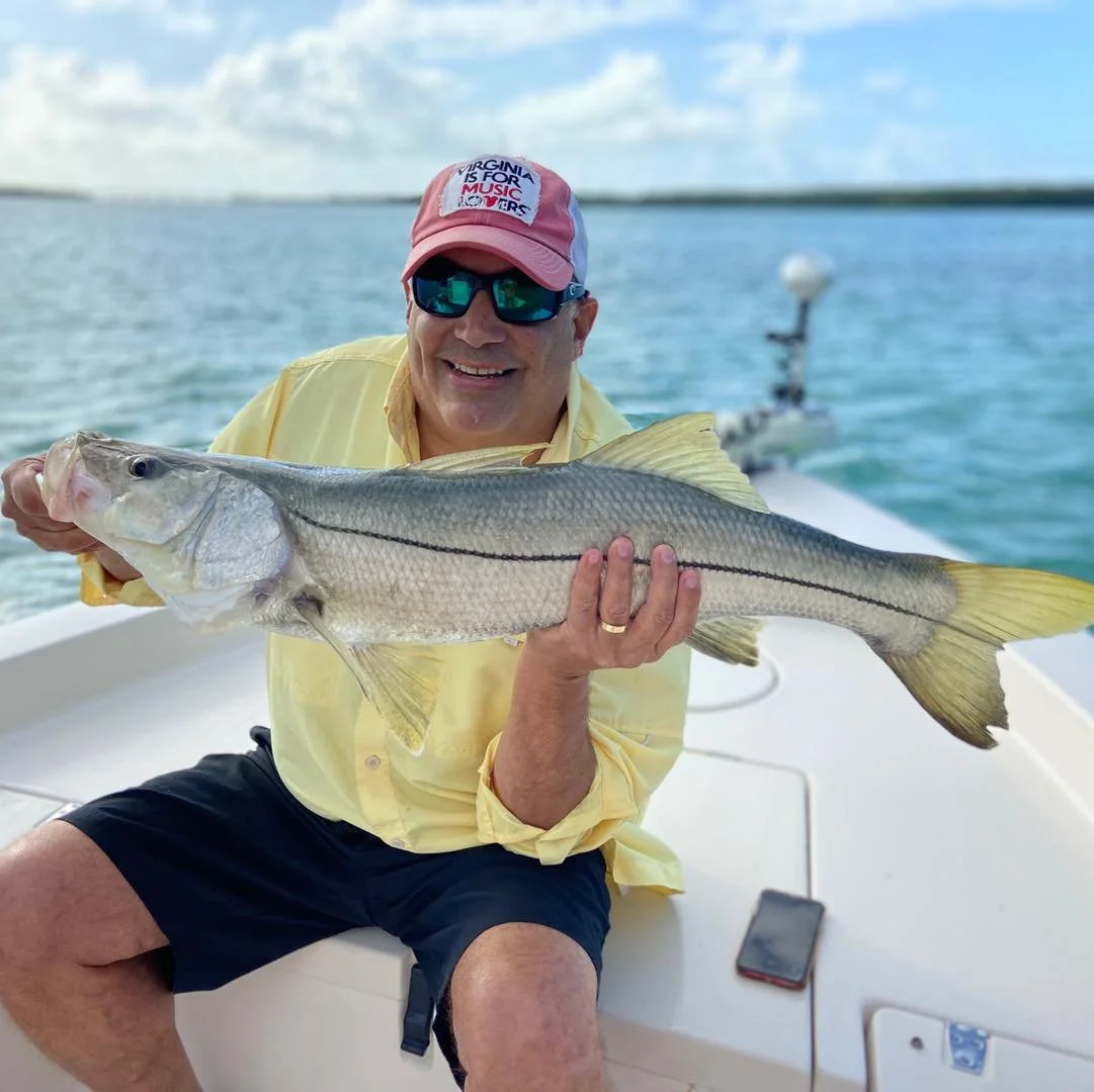Man in a yellow shirt and pink hat holding a large fish on a boat, with water and sky in the background.
