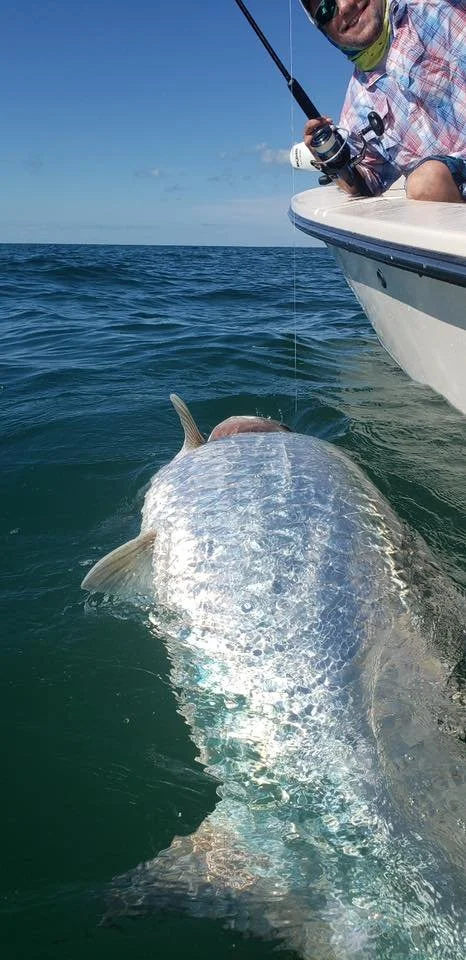 A man on a boat holding a fishing rod with a fish caught in the water.