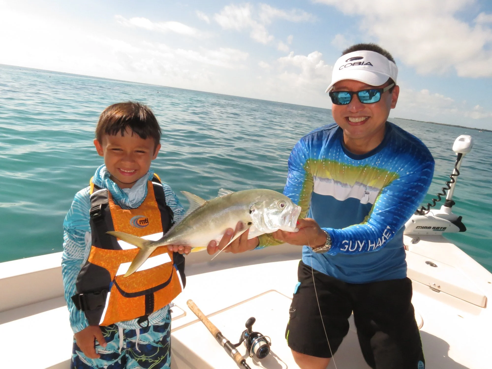 A man and a boy on a boat holding a fish caught while fishing in the ocean.