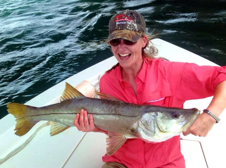 Woman in pink shirt holding a large caught fish on a boat at sea
