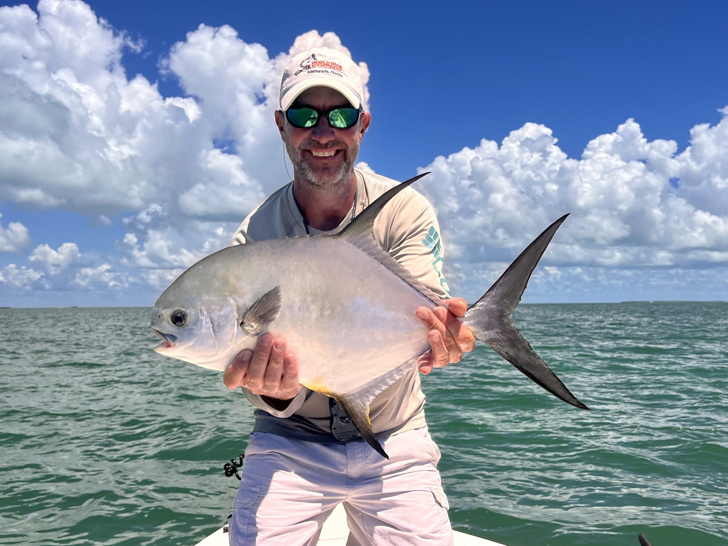 Man holding a permit on a boat in the ocean with a blue sky and clouds in the background.