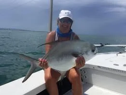 Child in a white cap and sunglasses holding a large fish on a boat in the water.
