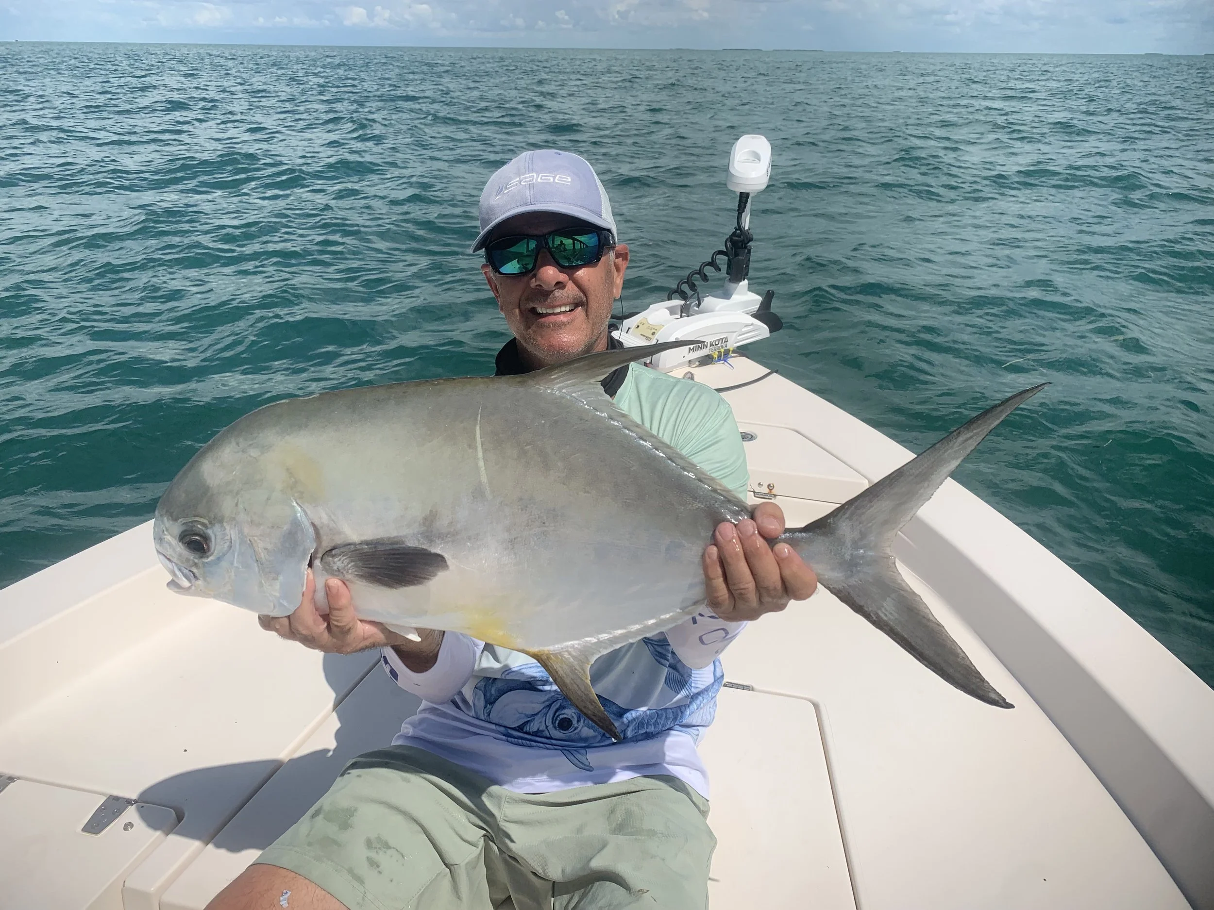 Man sitting on a boat holding a large fish with the ocean in the background.