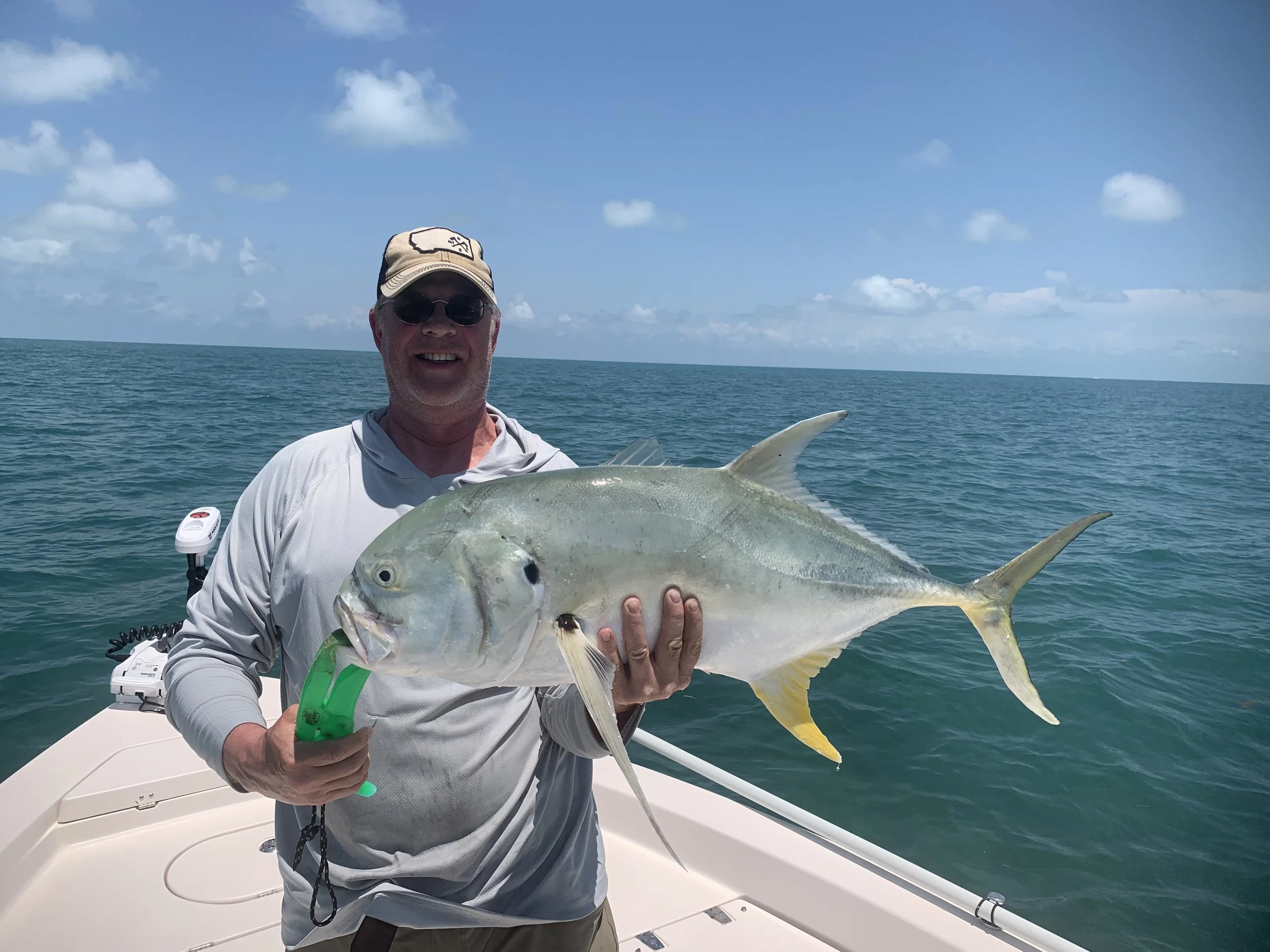 A man is smiling and holding a large fish on a boat in the ocean under a partly cloudy sky.