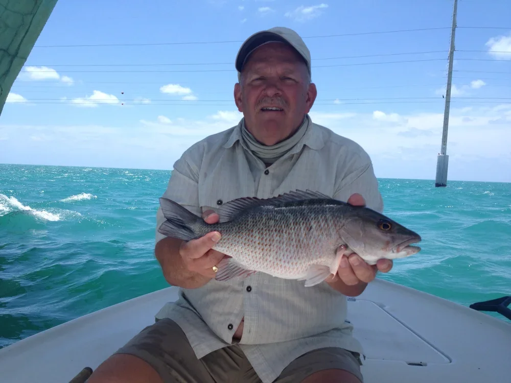 man in a light-colored shirt and cap holding a large fish on a boat in the ocean
