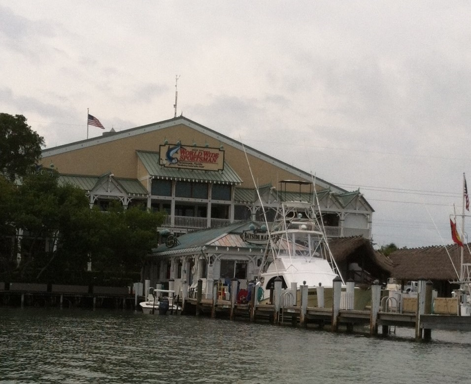 A marina with boats docked in front of a large, multi-story building with a sign reading 'World Wide Sportsman'.
