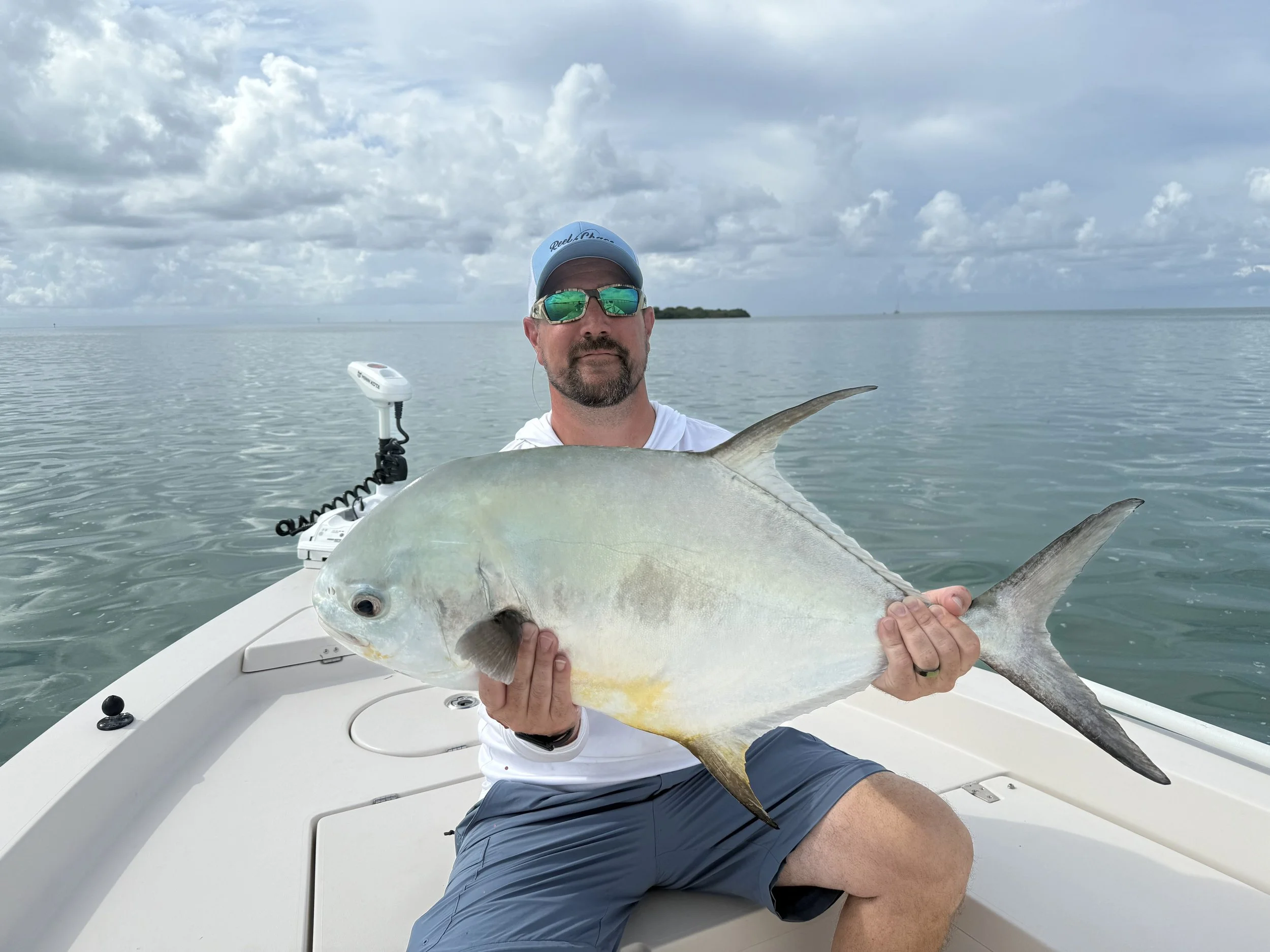 Man holding a large fish on a boat in open water under cloudy sky.