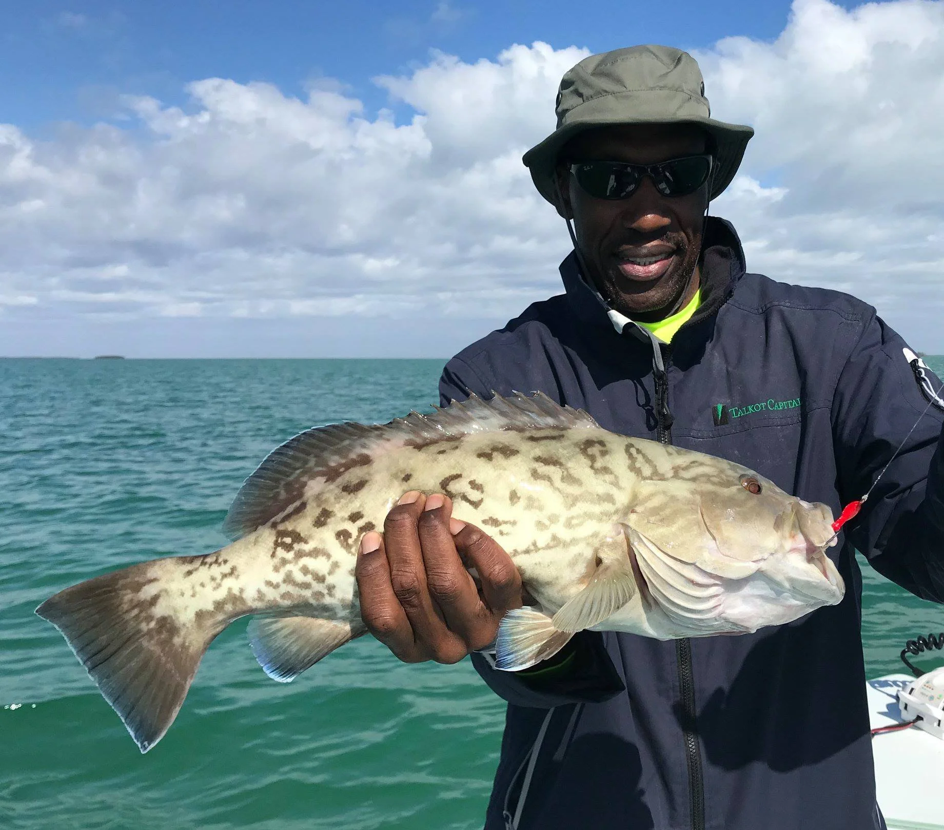 Man holding a large spotted fish on a boat with water and cloudy sky in the background.