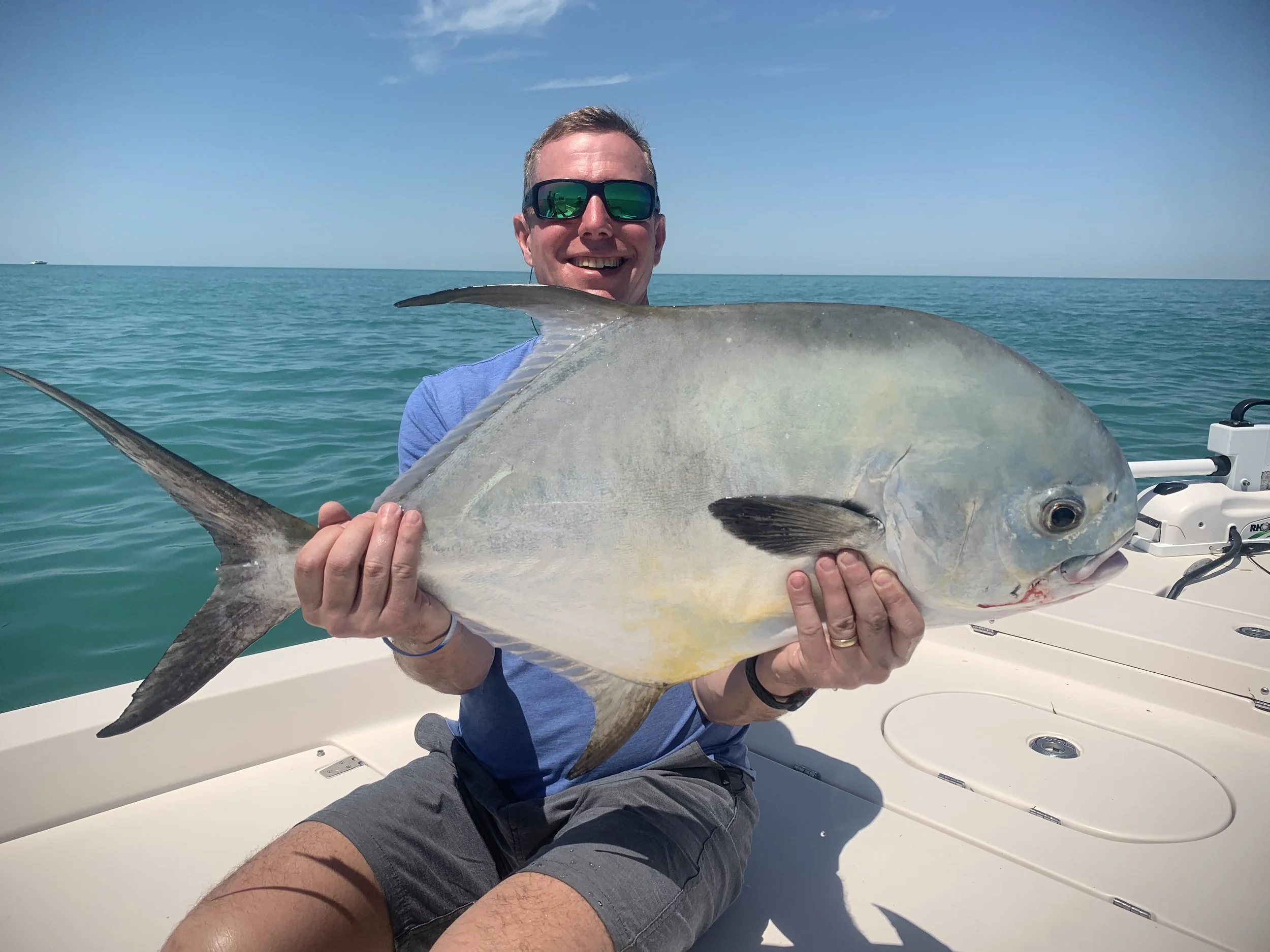 A man holding a large fish on a boat with the ocean in the background.