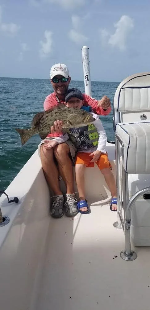 A man and a boy on a boat holding a large fish they caught.