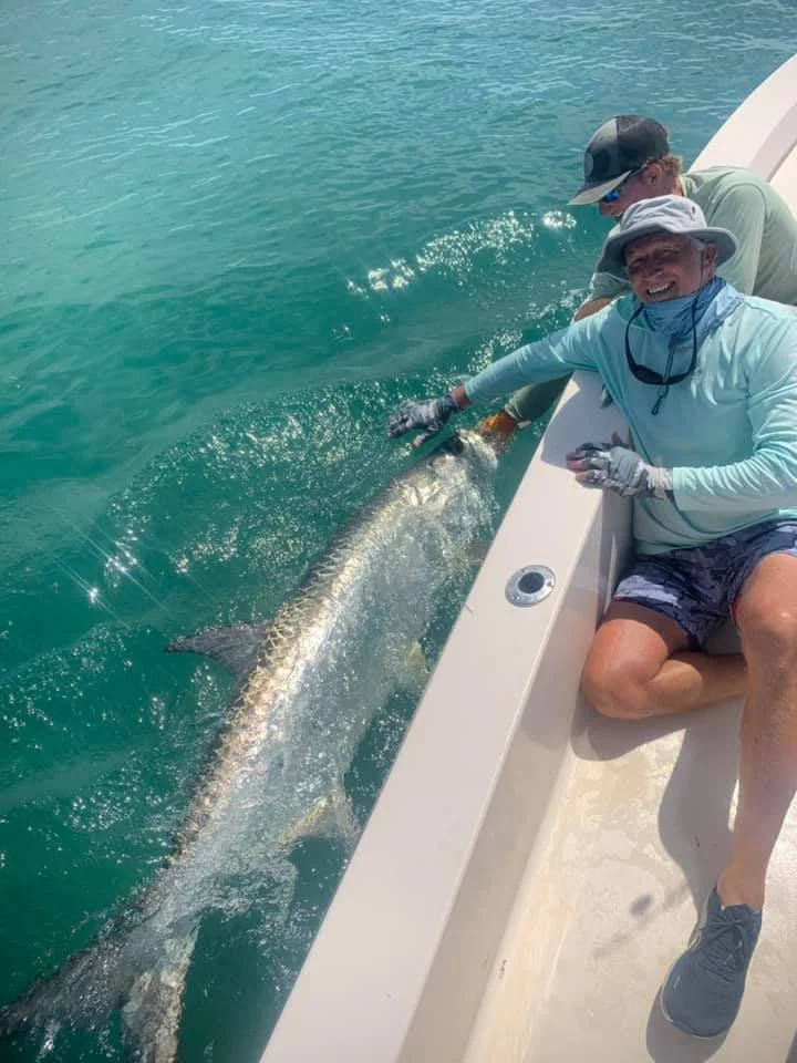 Two men on a boat releasing a large fish into the water.