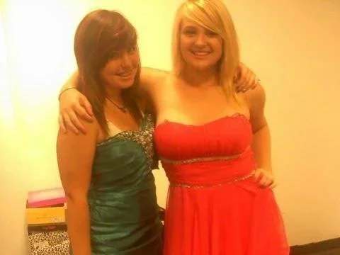 Two young women smiling and posing with their arms around each other, dressed in formal dresses.