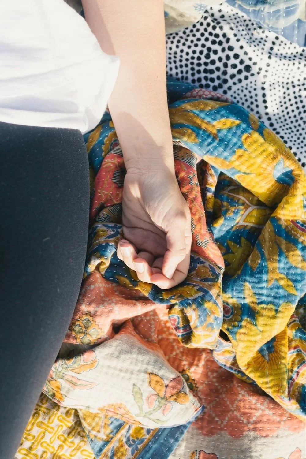 Close-up of a person's hand resting on their lap, with colorful, patterned fabric and floral textile around.