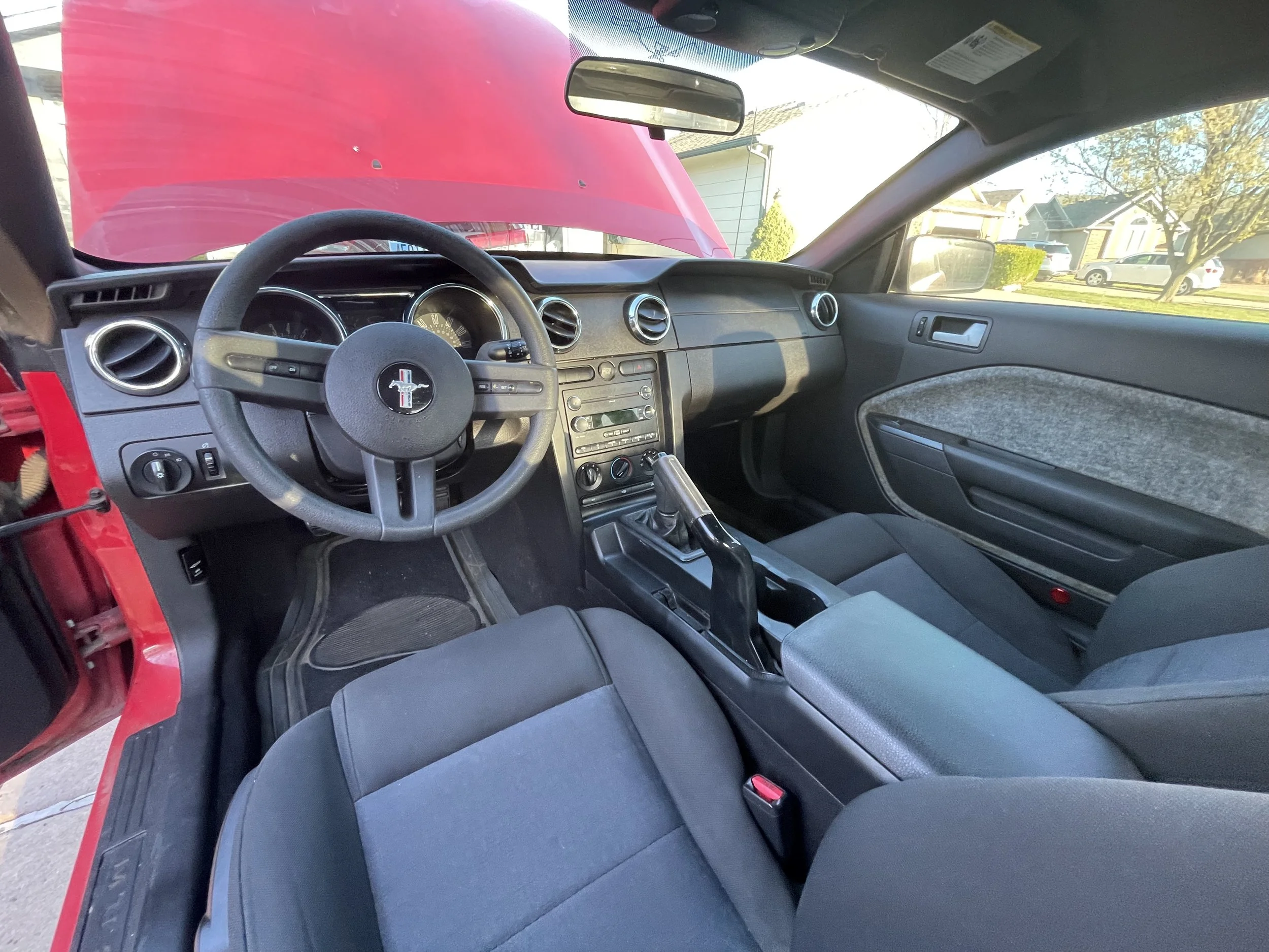 Interior of a red Ford Mustang car showing the steering wheel, dashboard, gear shift, and front seats.