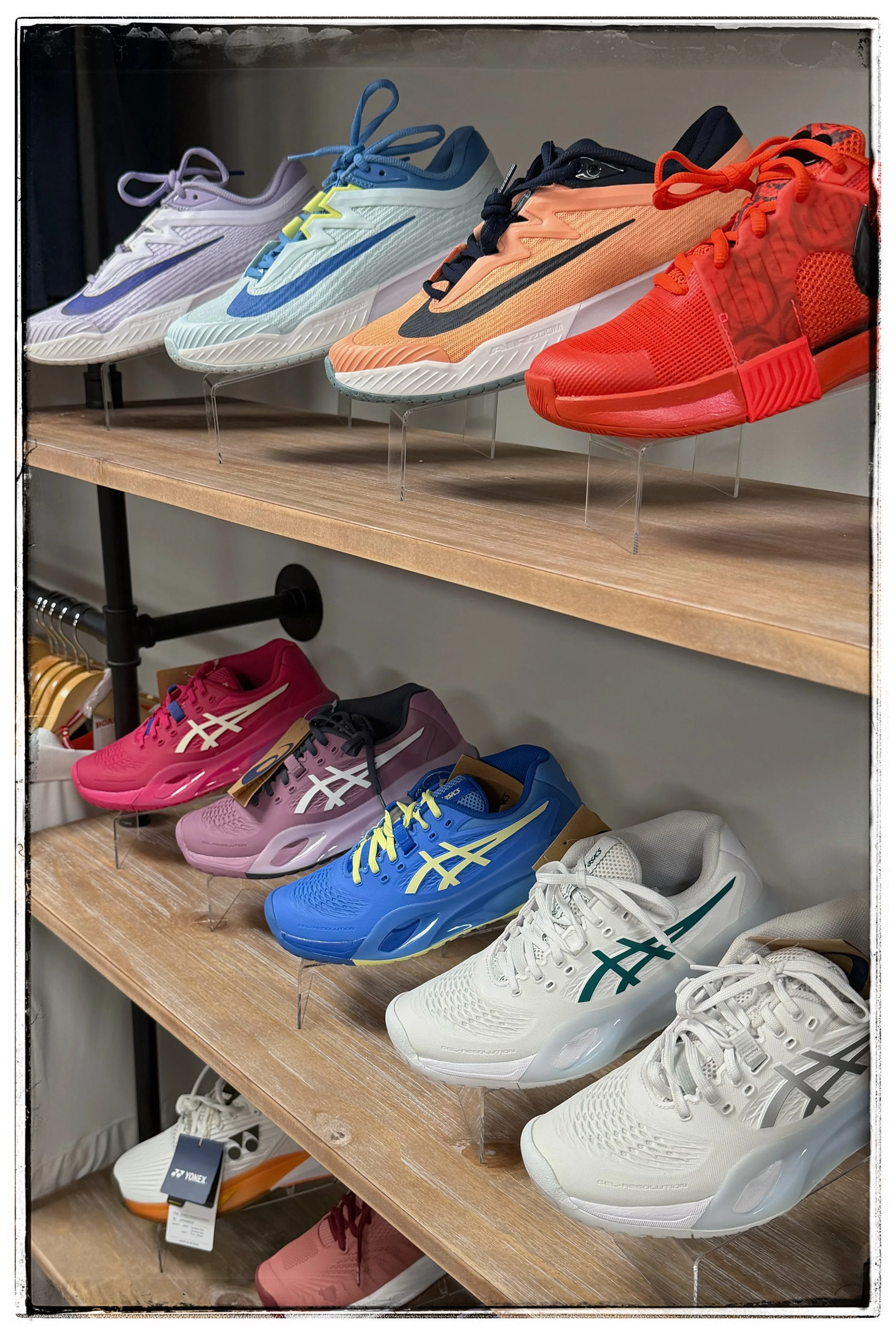 Display of various athletic shoes on wooden shelves, including models in white, purple, blue, orange, red, pink, blue with yellow accents, and white with teal accents.