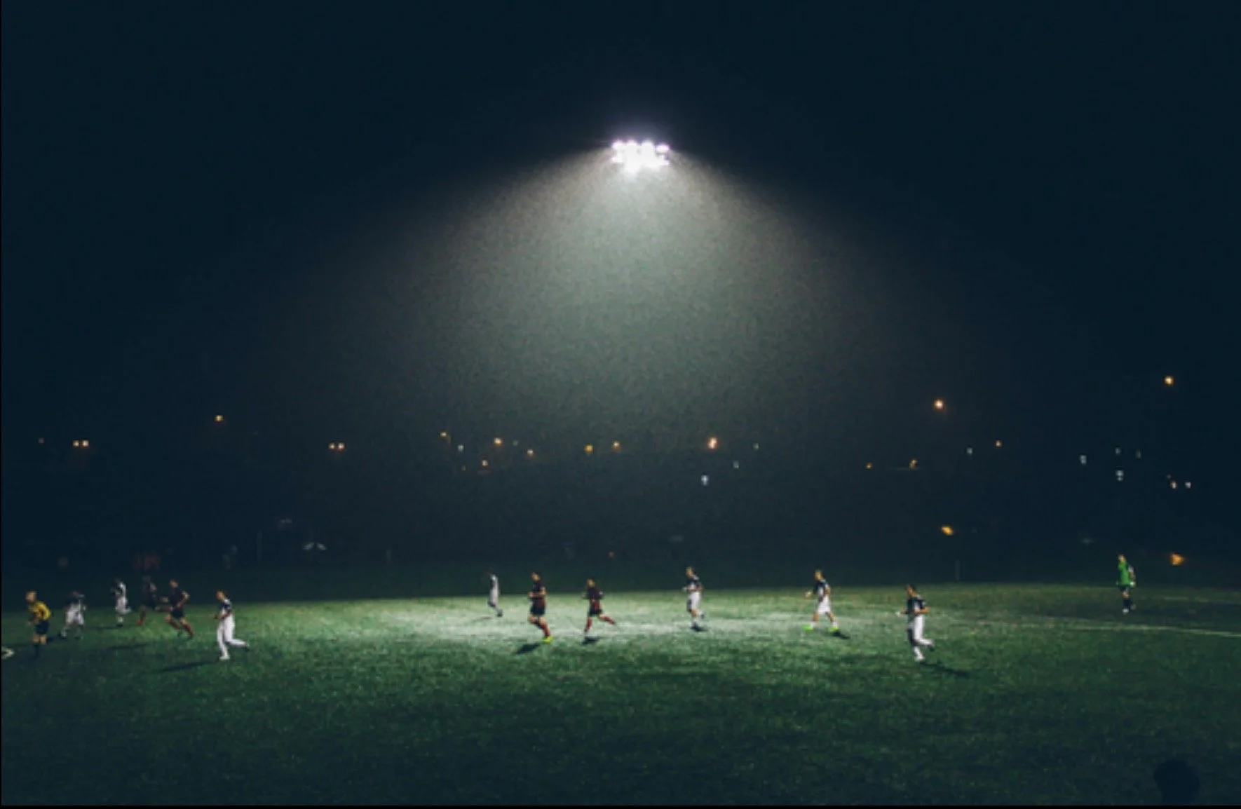 Soccer match under stadium lights at night with players on the field.