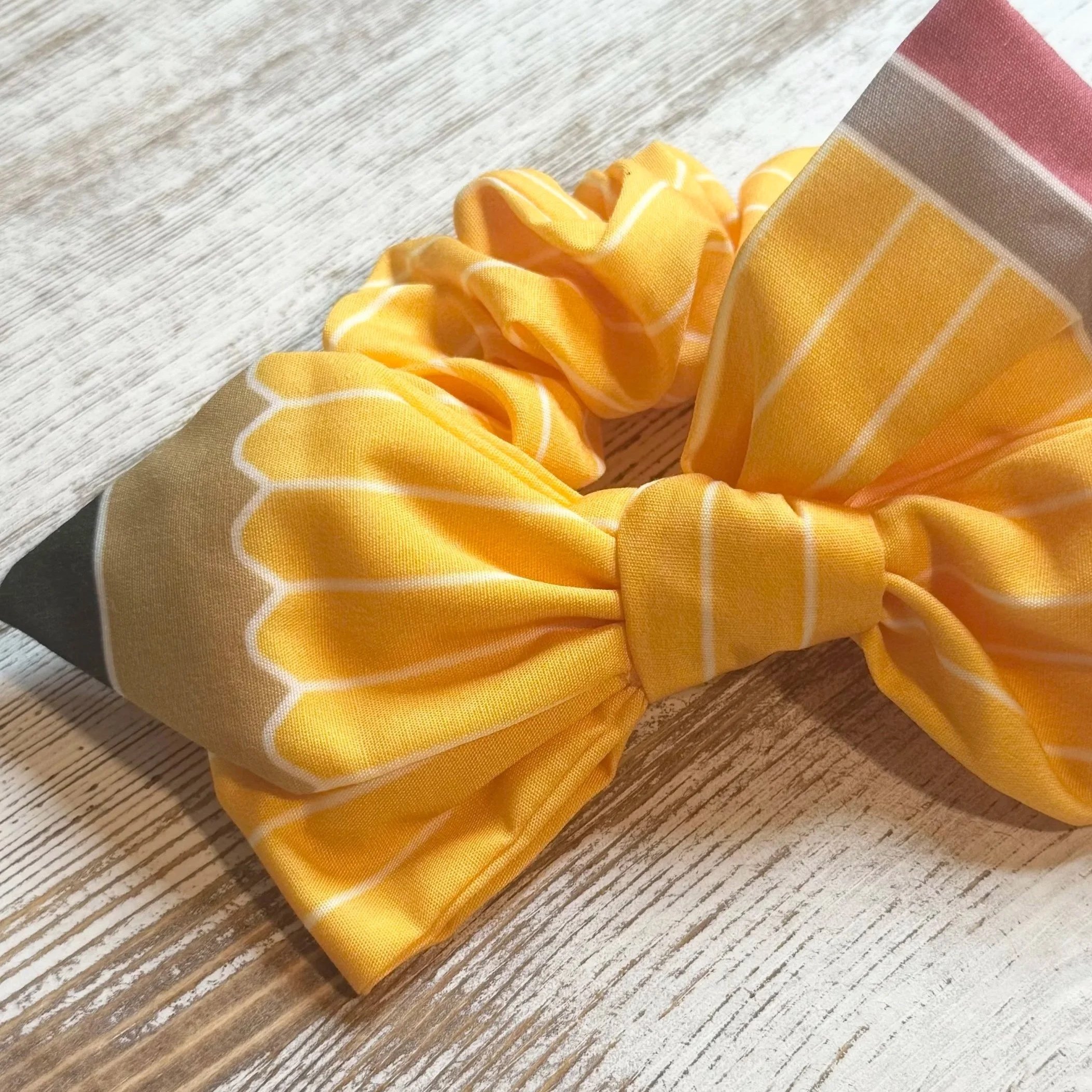 Yellow patterned fabric hair scrunchie on a wooden surface.