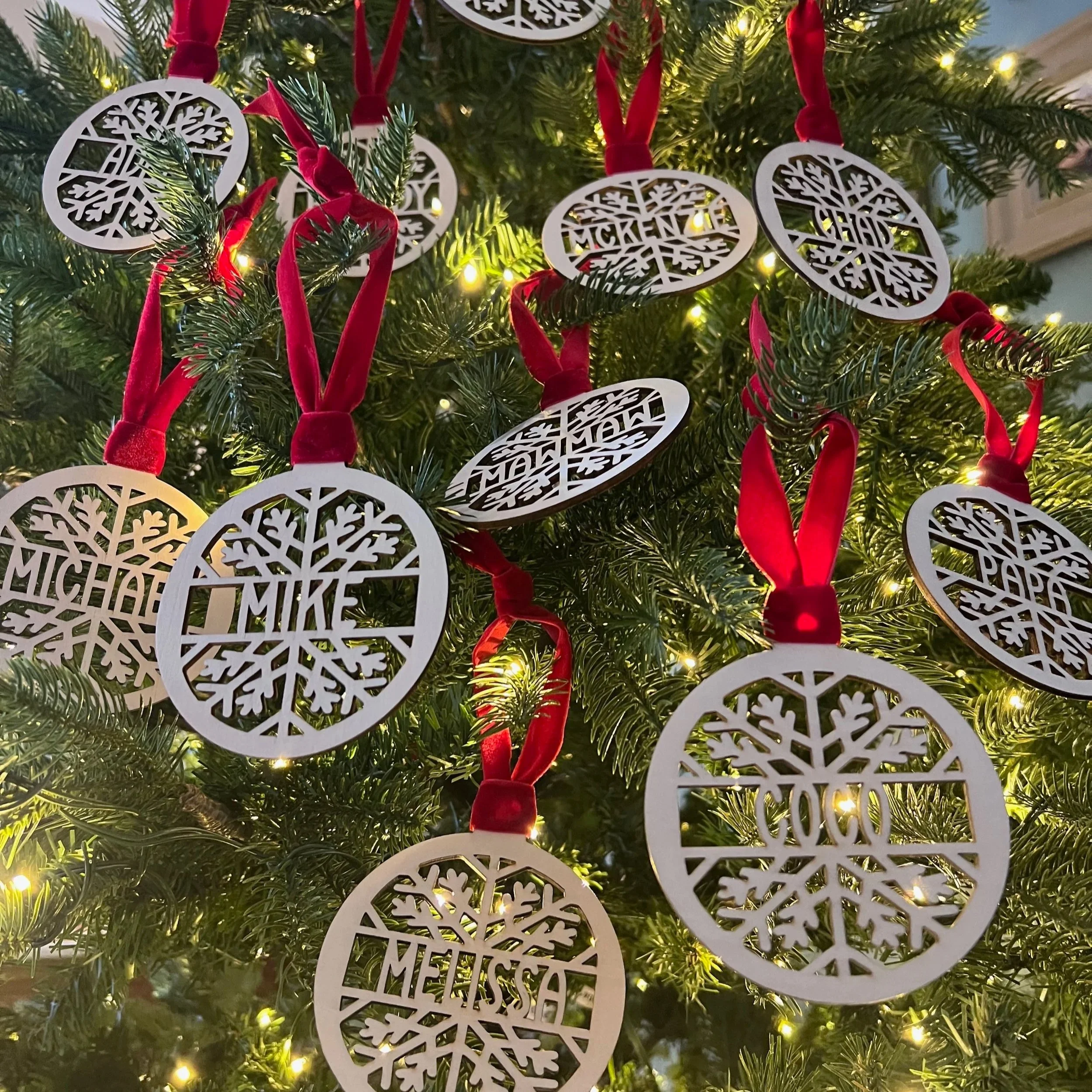 Christmas tree decorated with white snowflake ornaments with names and red ribbons.