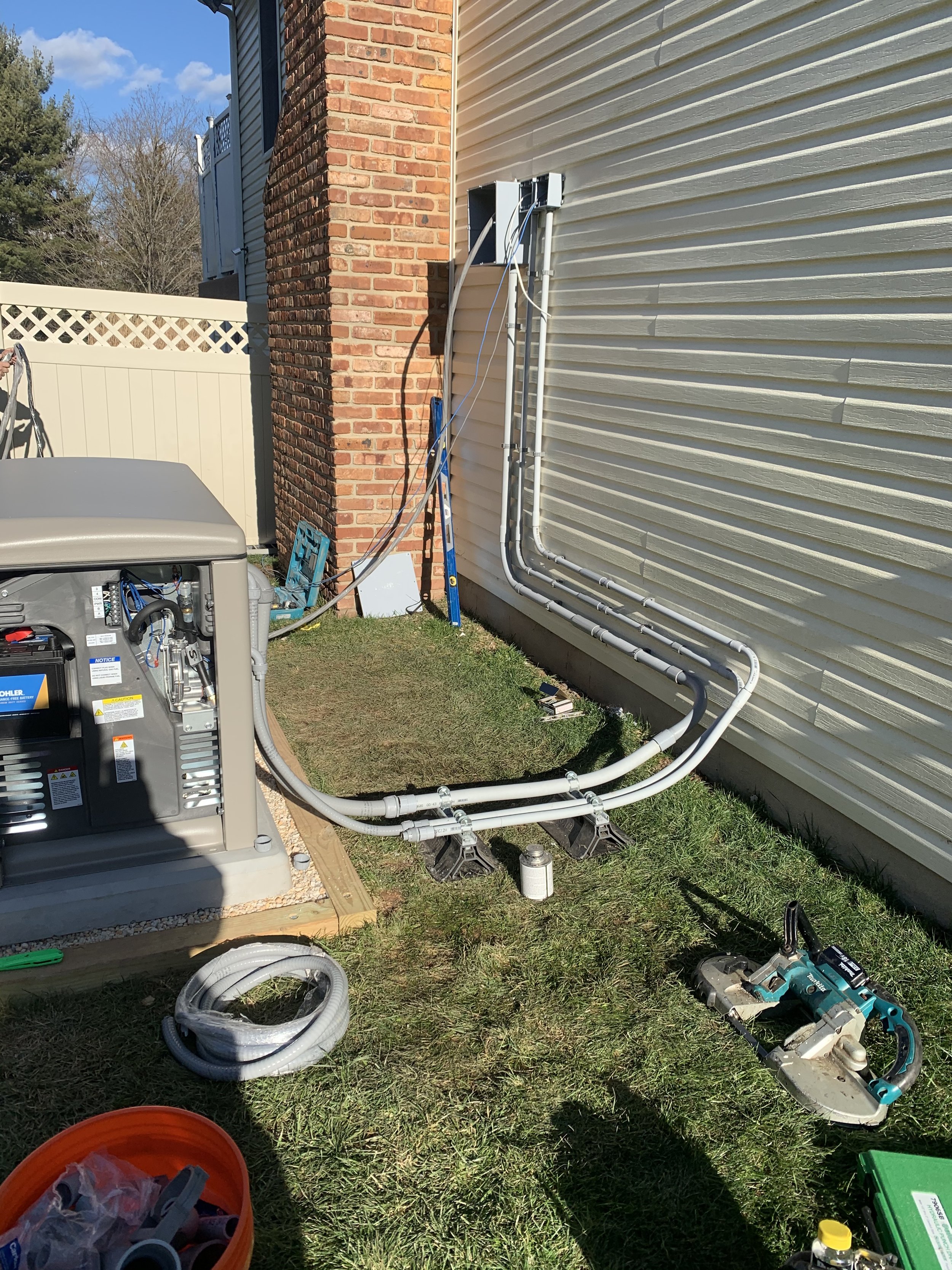 Installing new electrical or HVAC conduits outside a house with tools and equipment on the ground.