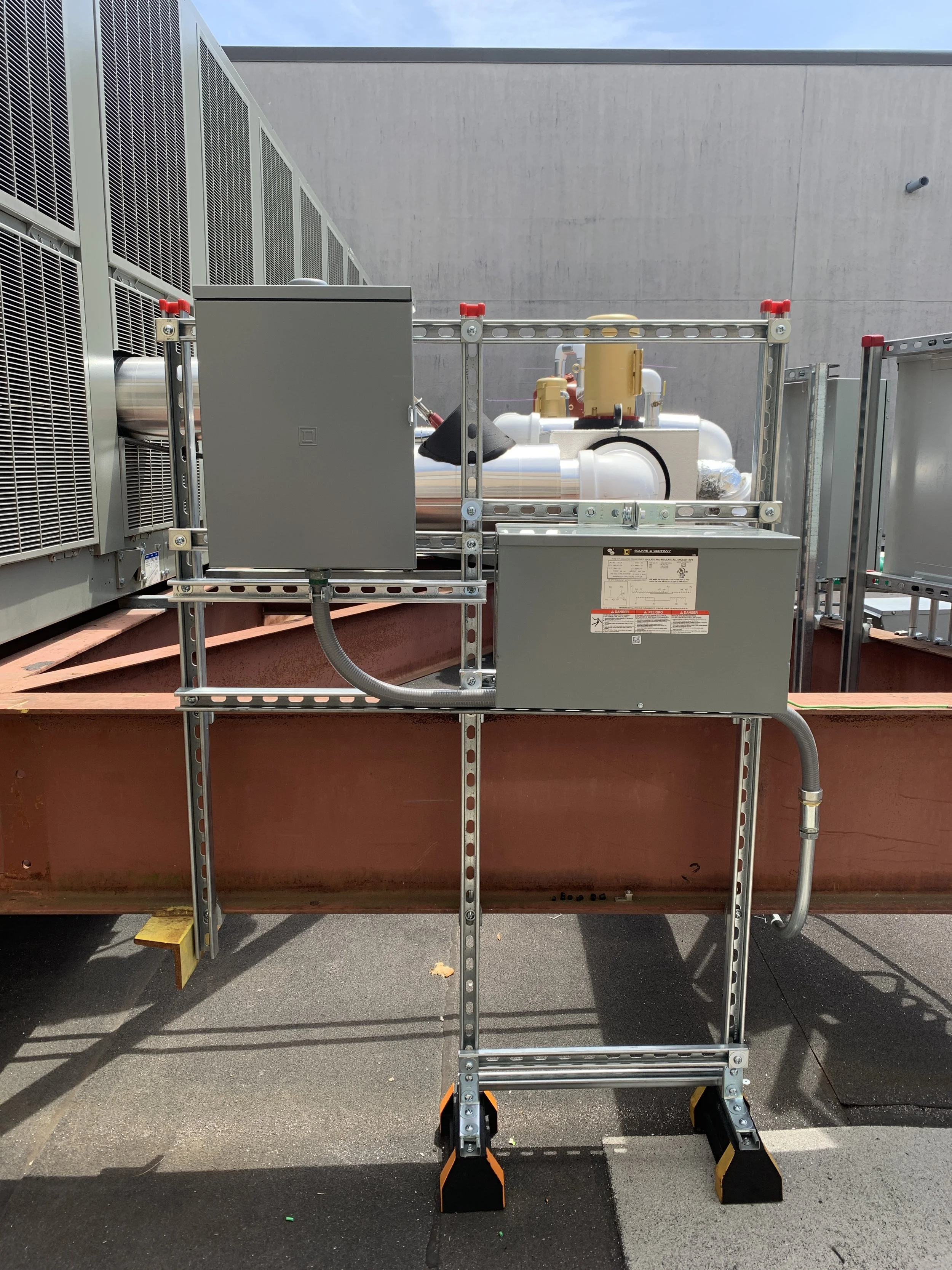 Industrial HVAC equipment with metal framework, piping, and electrical panels on a rooftop.