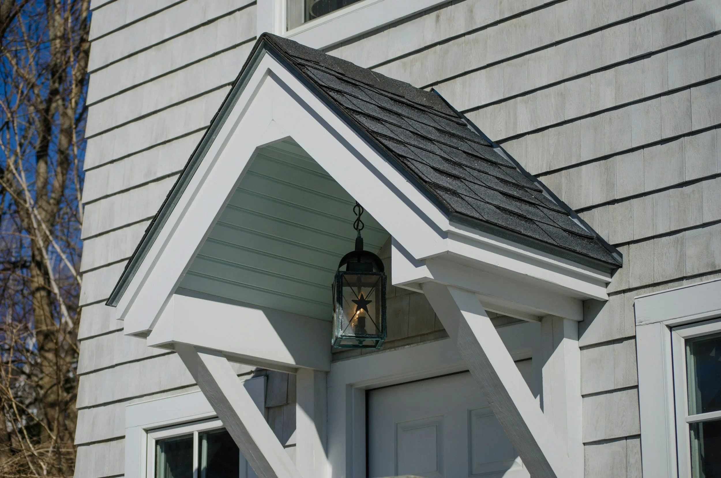 Close-up of a house's front entrance with a small gabled roof, an outdoor lantern, and white siding.