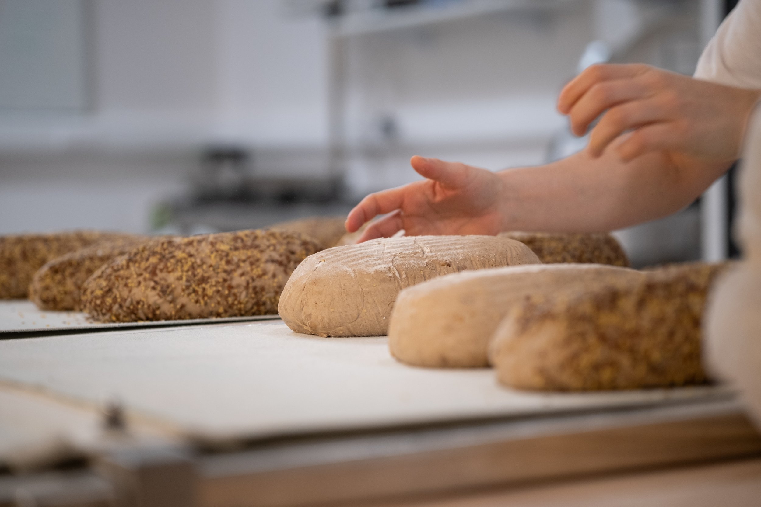 Person working with several loaves of bread on a white work surface in a bakery or kitchen.