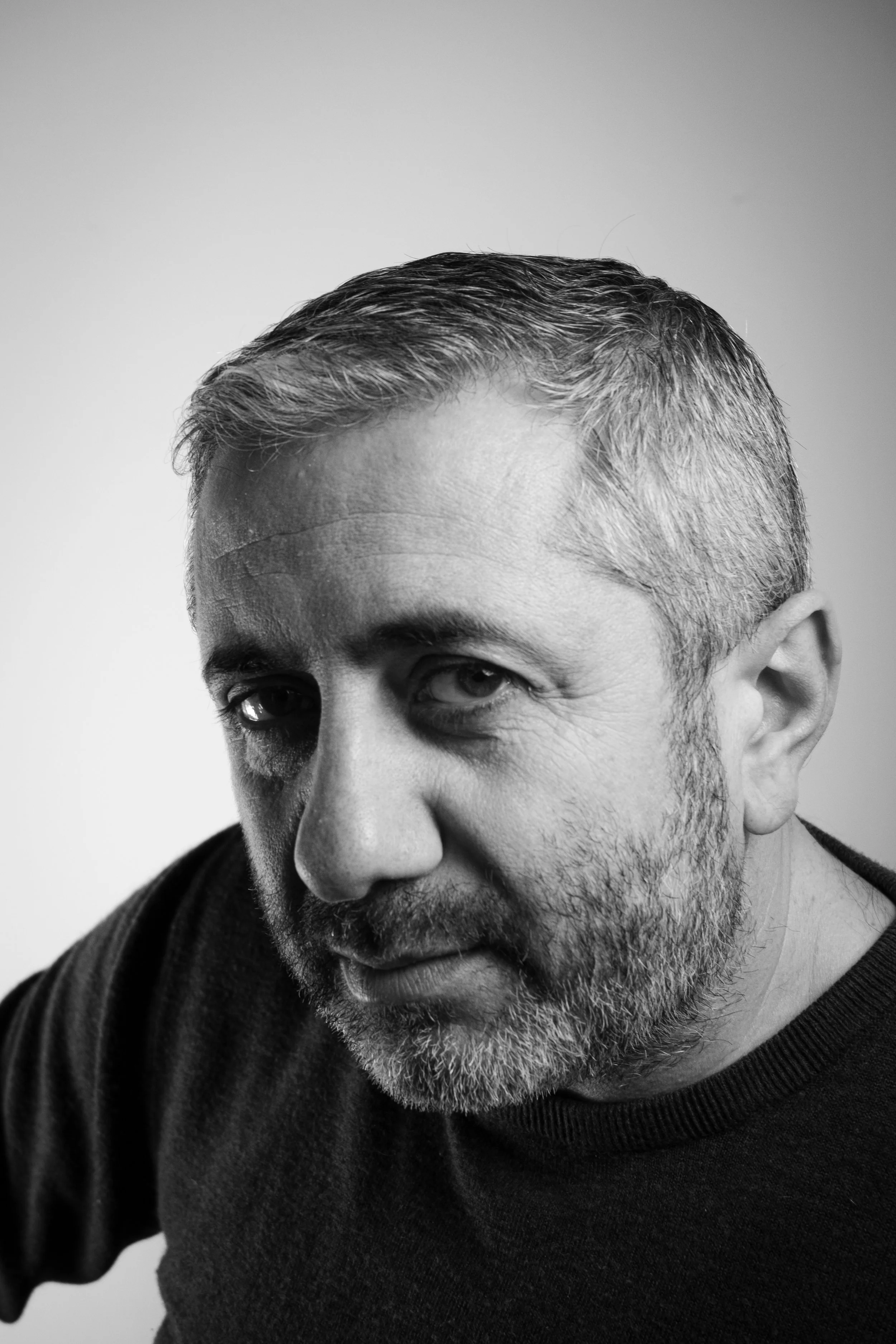 Black and white portrait of a middle-aged man with short, graying hair and a beard, wearing a dark shirt, looking at the camera.