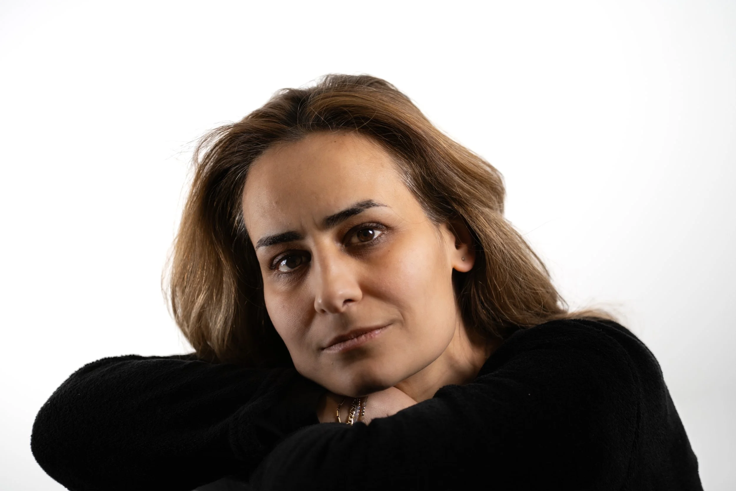 Portrait of a woman with brown hair and brown eyes resting her head on her crossed arms, looking into the camera with a serious expression.