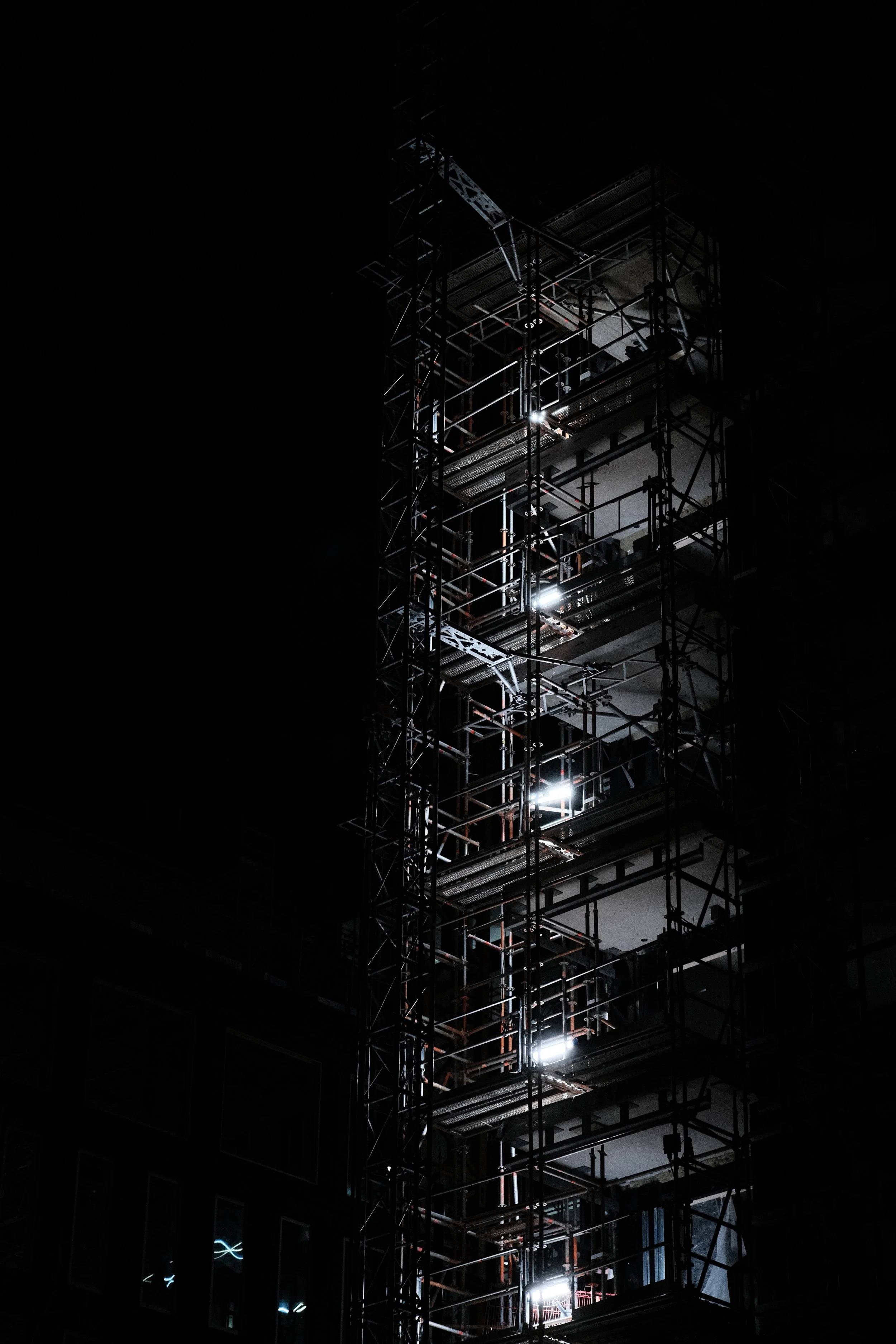 Night view of a construction elevator surrounded by scaffolding on a building under construction or renovation.