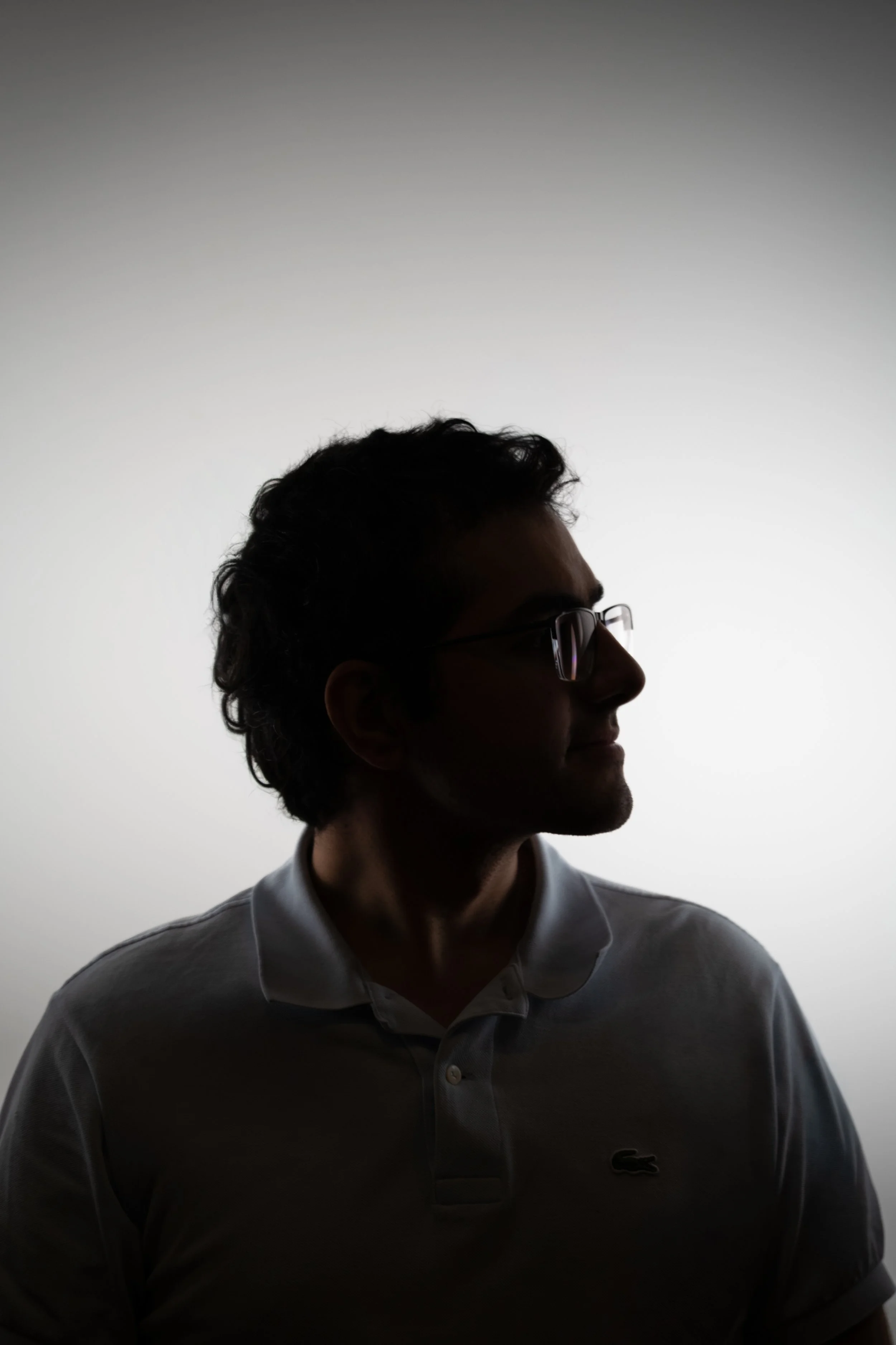 Silhouette of a man wearing glasses and a collared shirt, facing sideways against a plain, gradient background.