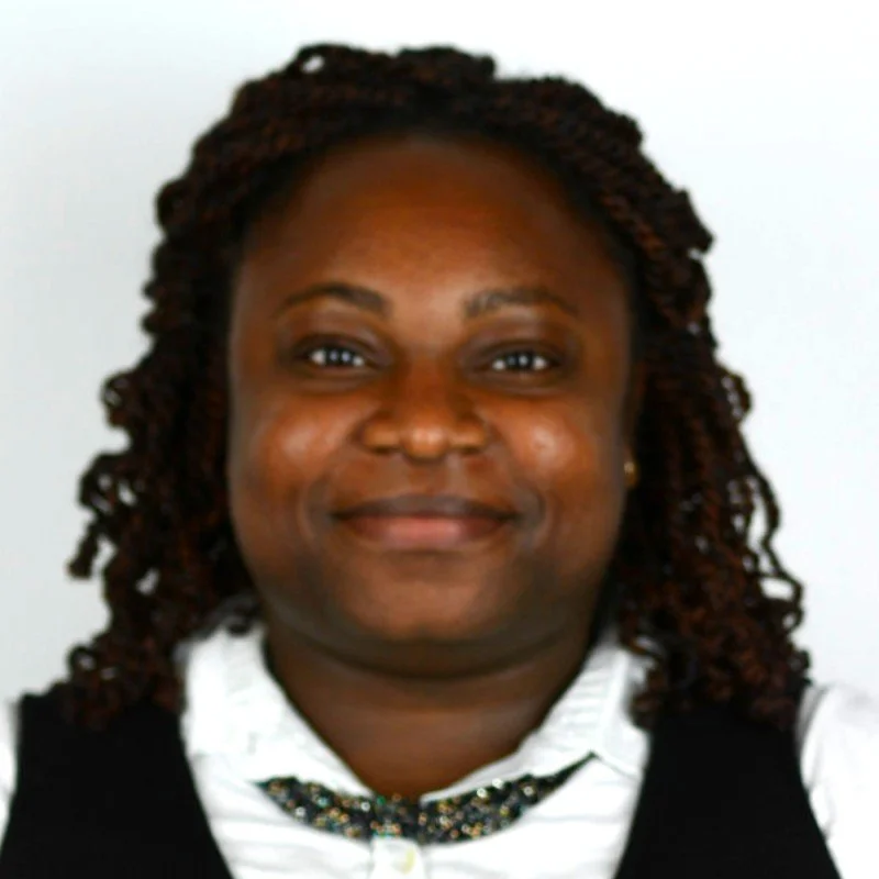 Close-up of a smiling woman with shoulder-length braids, wearing a white shirt and a patterned necklace, against a white background.
