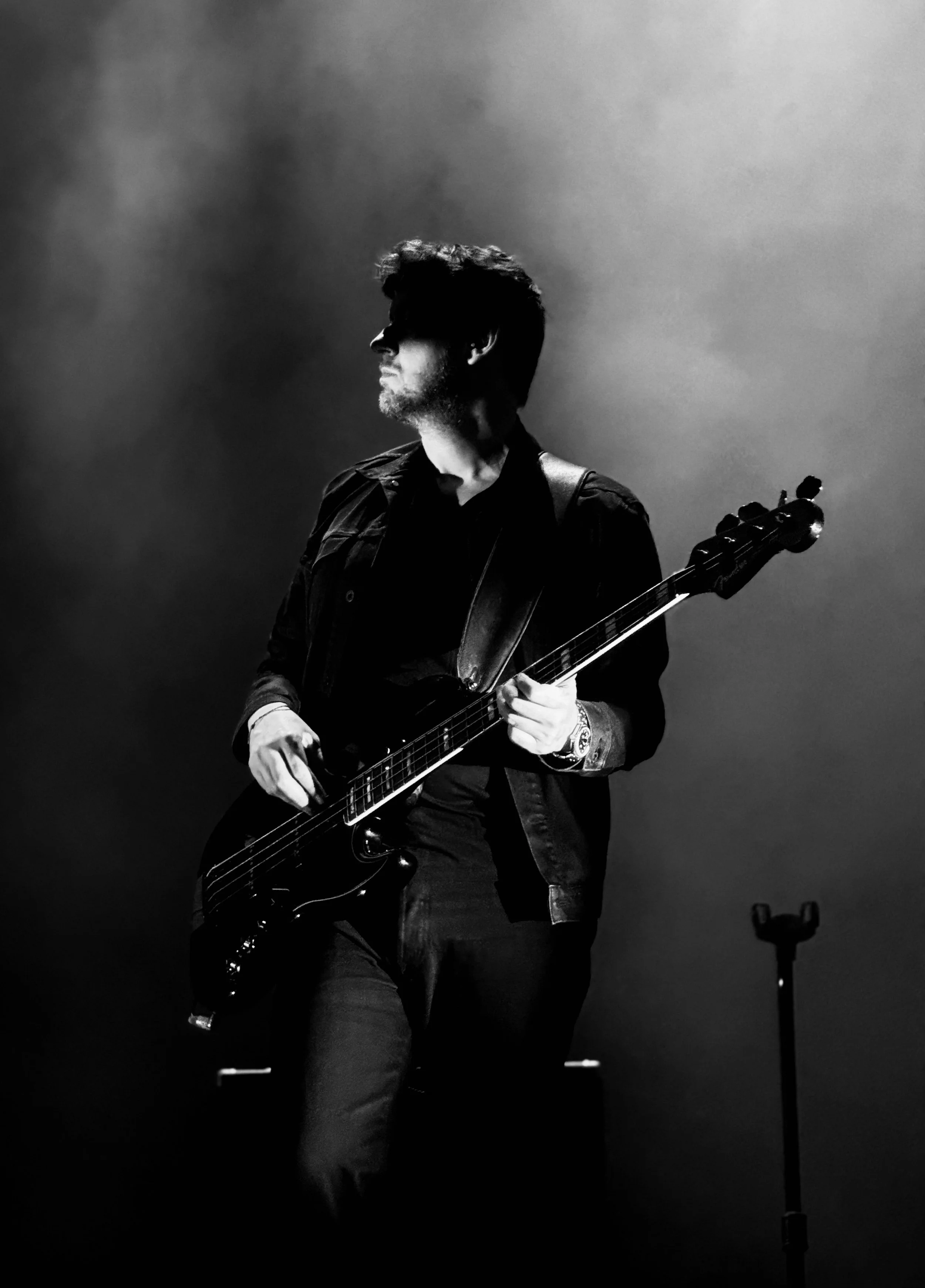 A man holding a guitar on stage, with dim lighting and a hazy background.