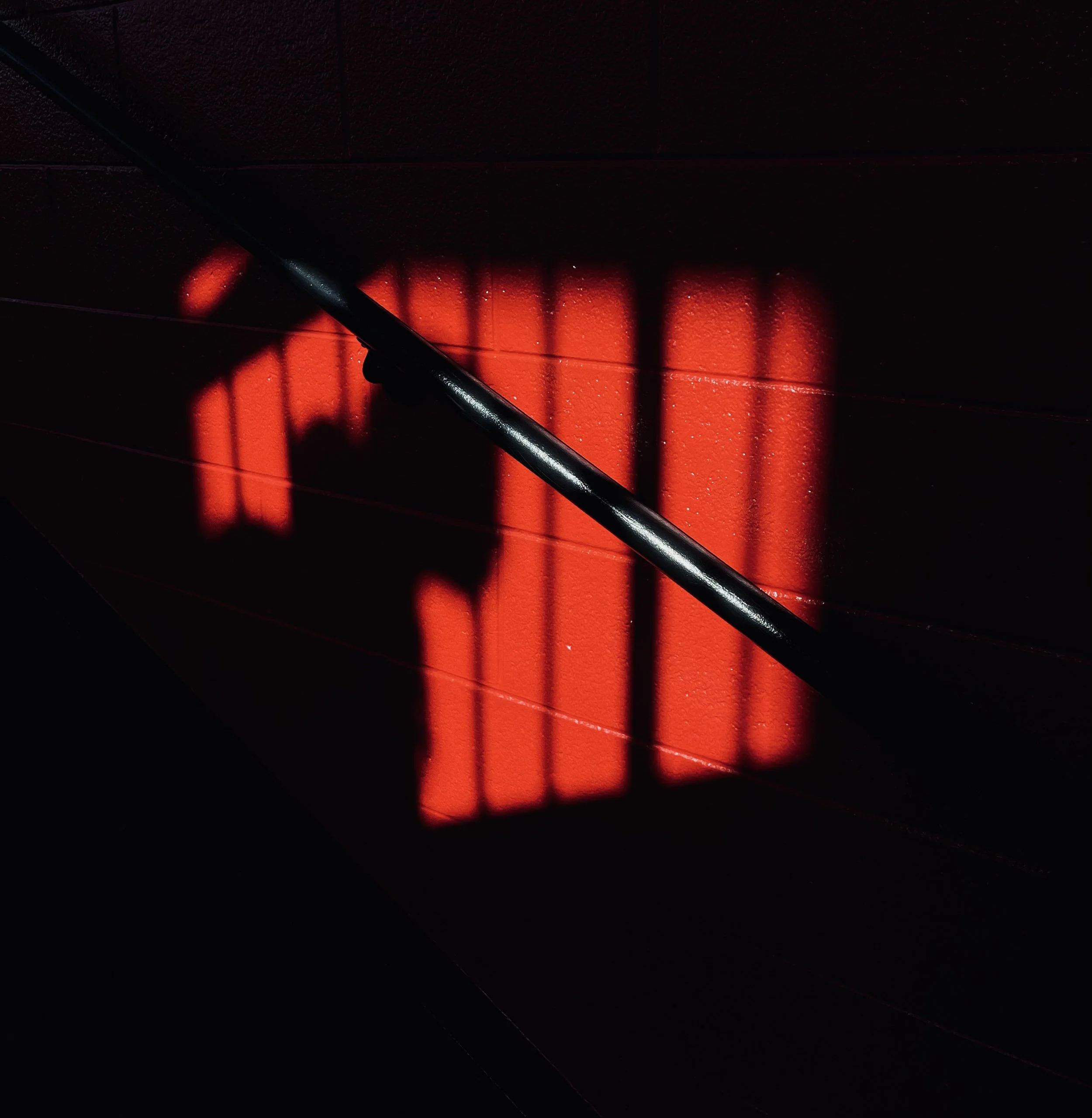 Shadow of a chair back cast on a red painted wall.