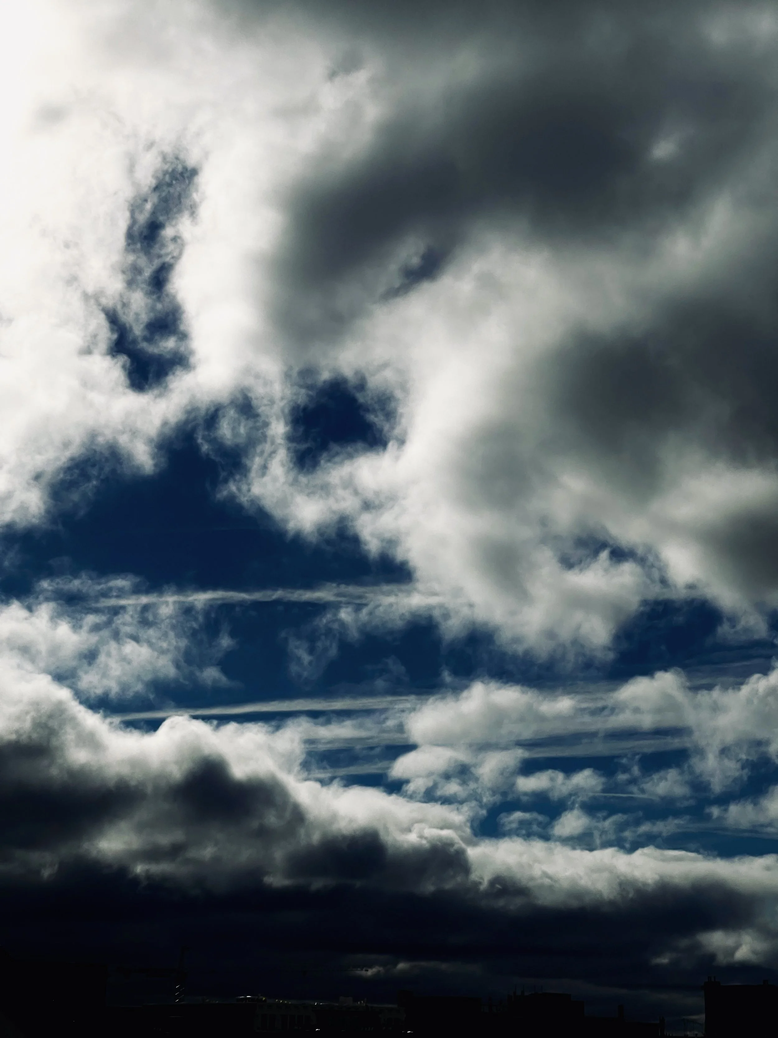 Dark storm clouds in a cloudy sky over a city skyline.