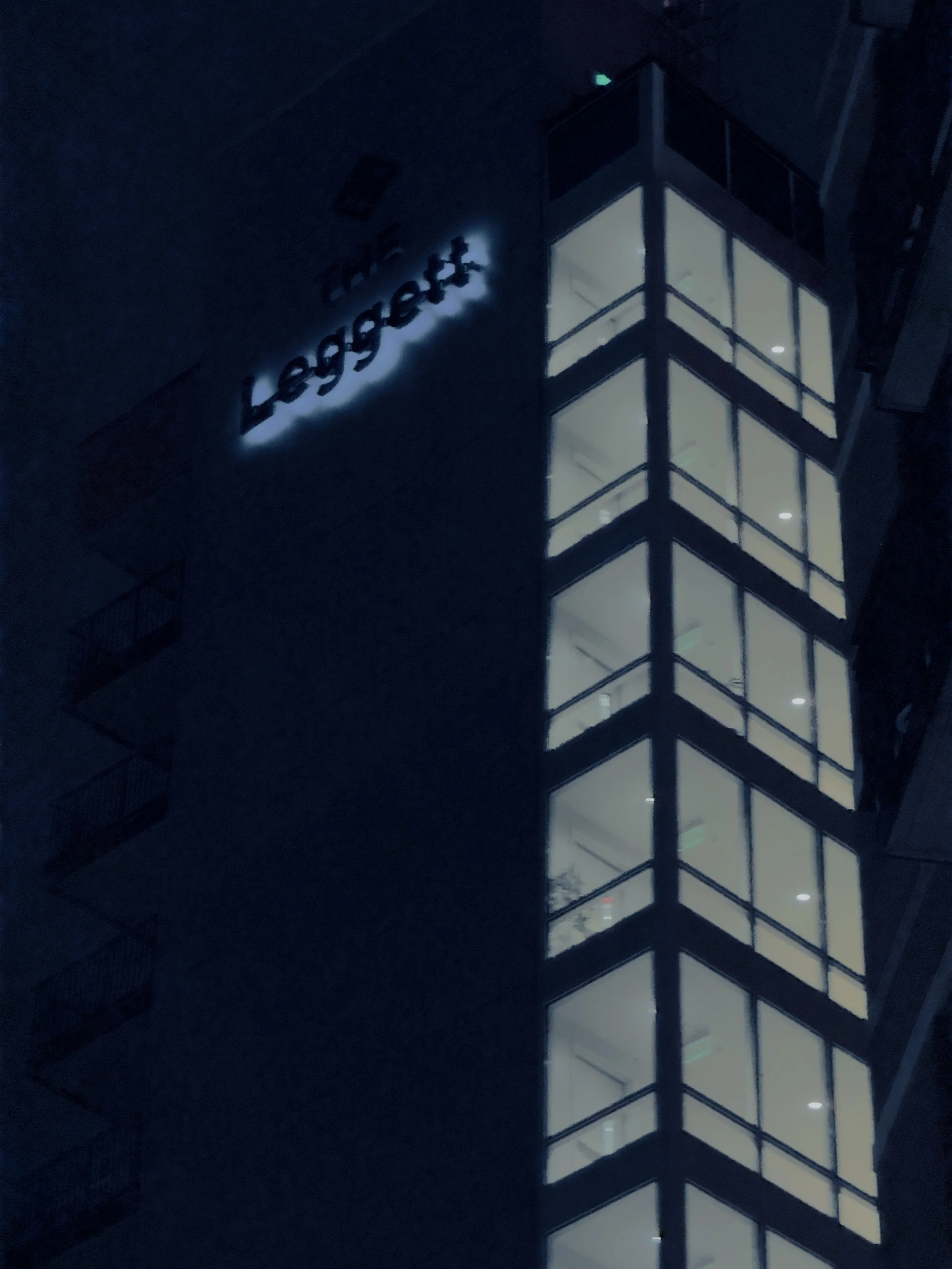 Night view of a modern building with illuminated windows and a sign that reads 'The Leggeret' on the dark exterior wall.