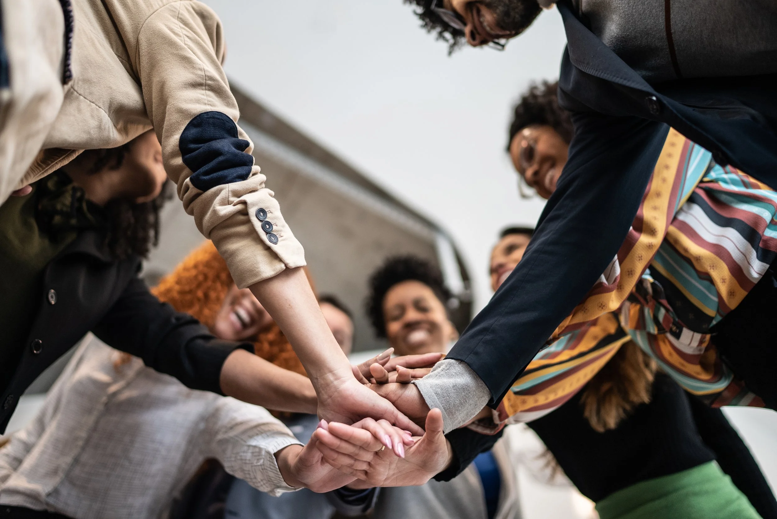 A group of diverse people in a circle placing their hands together in a show of teamwork and unity.
