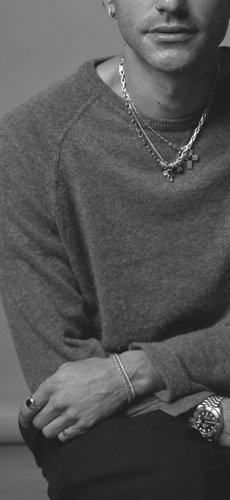 Close-up of a person wearing a dark sweater, multiple necklaces including a cross, a bracelet, and a watch, with their arms crossed. Jean-Pierre Sosa