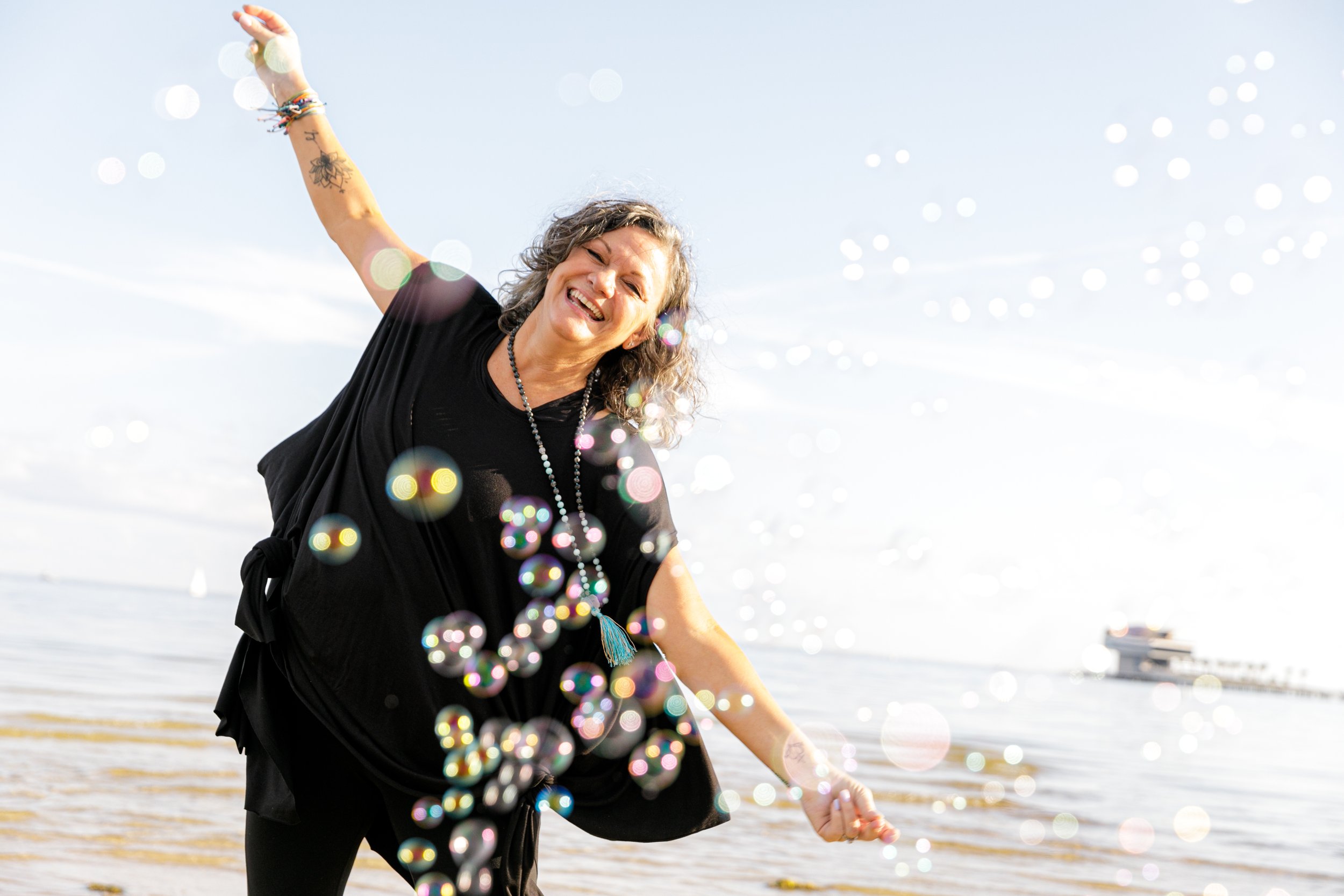A woman smiling and playing with bubbles on the beach during daytime.