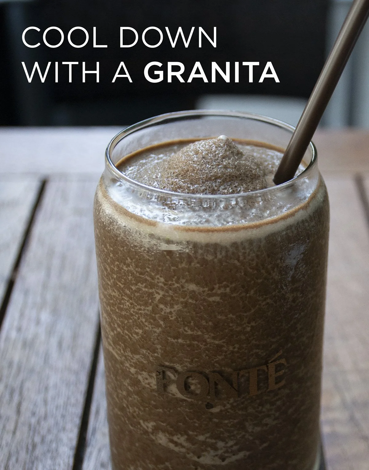 A glass of iced coffee with a straw, topped with whipped foam, on a wooden table, with text overlay that reads 'Cool down with a granita.'