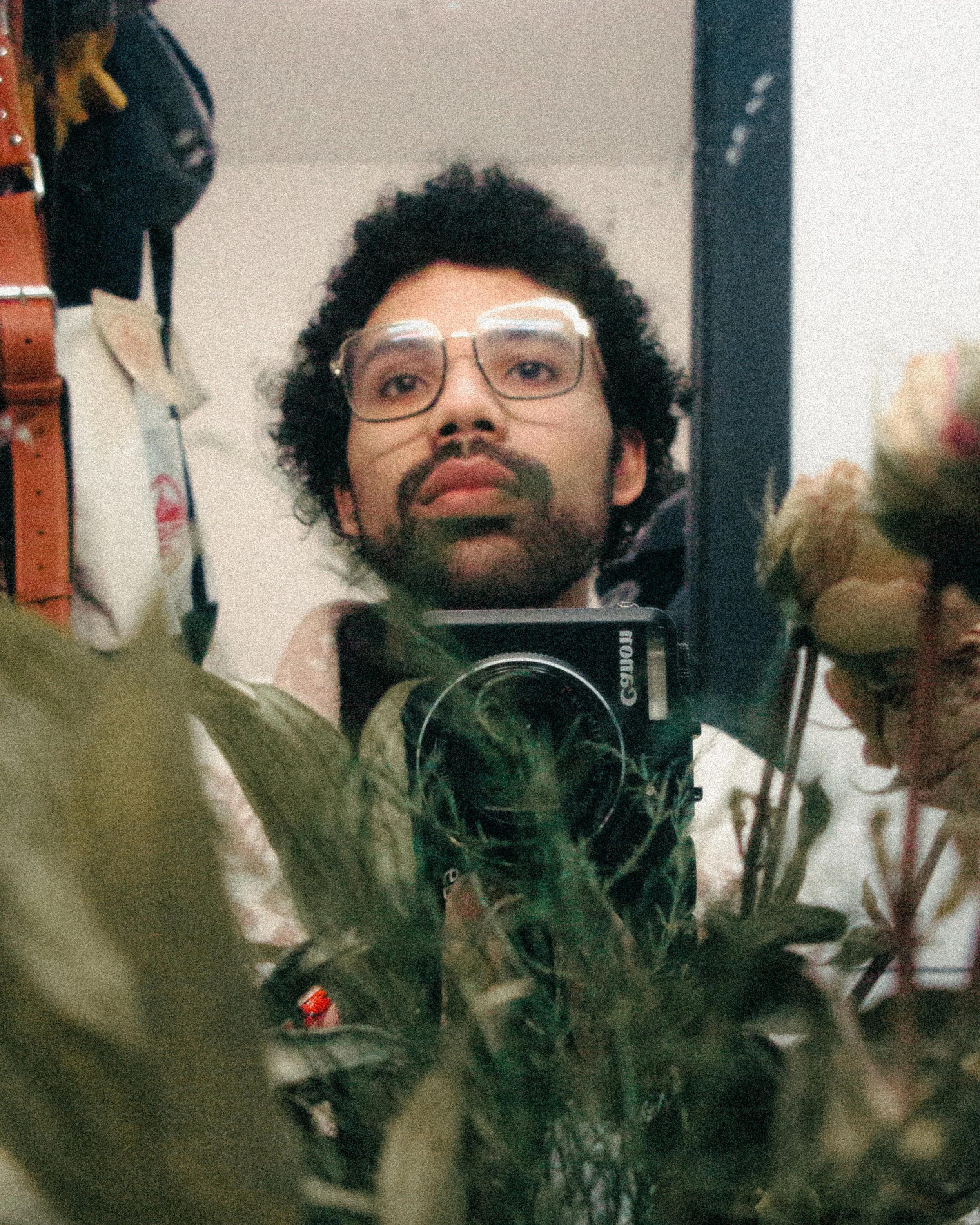 A man with glasses and a beard takes a selfie in a mirror surrounded by flowers.