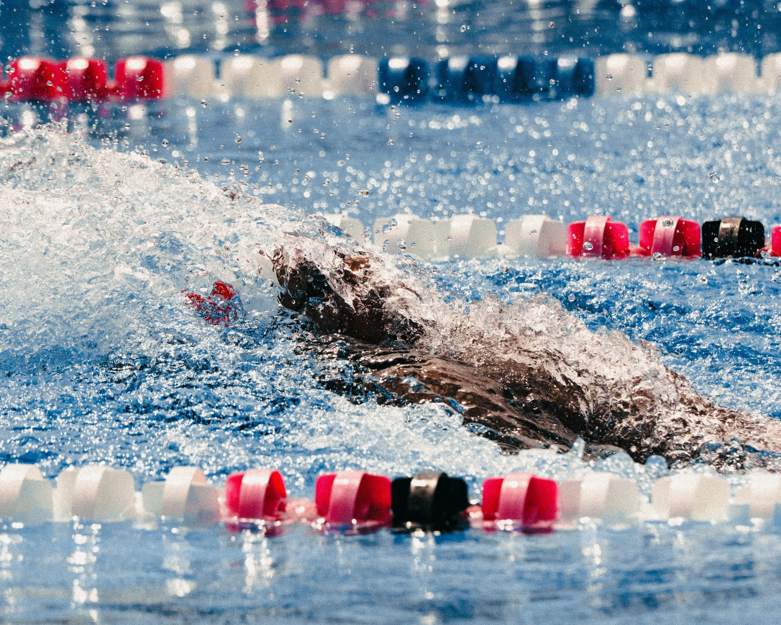 Swimmer performing a stroke in a swimming pool, with lane dividers in the background.