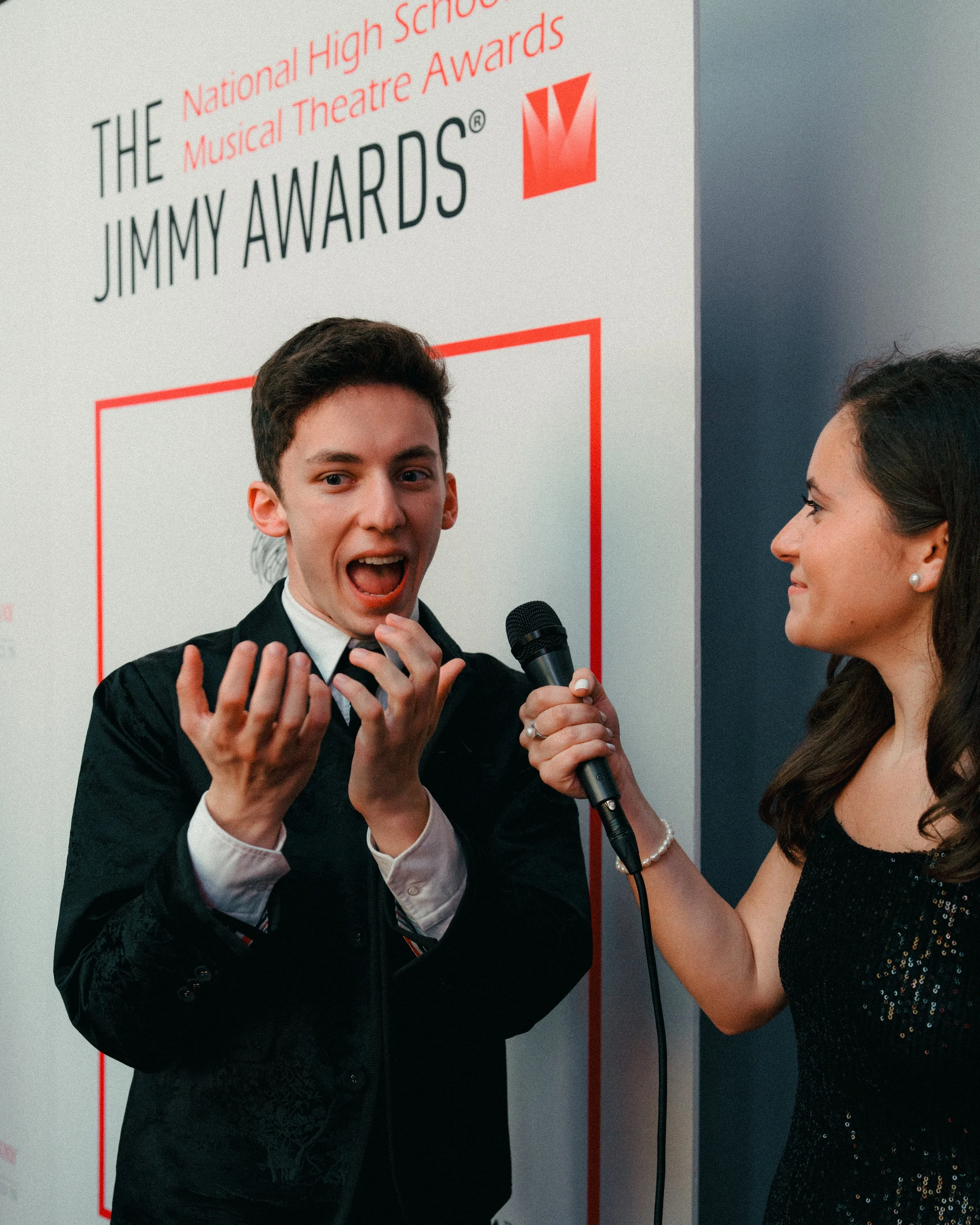 A young man in formal attire being interviewed with a microphone at the Jimmy Awards event.