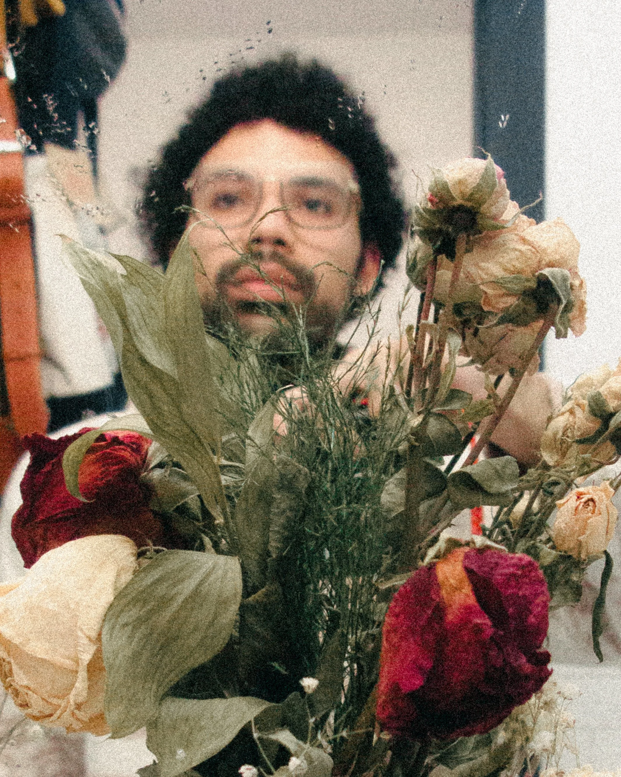 Person with glasses and curly hair behind a bouquet of dried, wilted flowers.