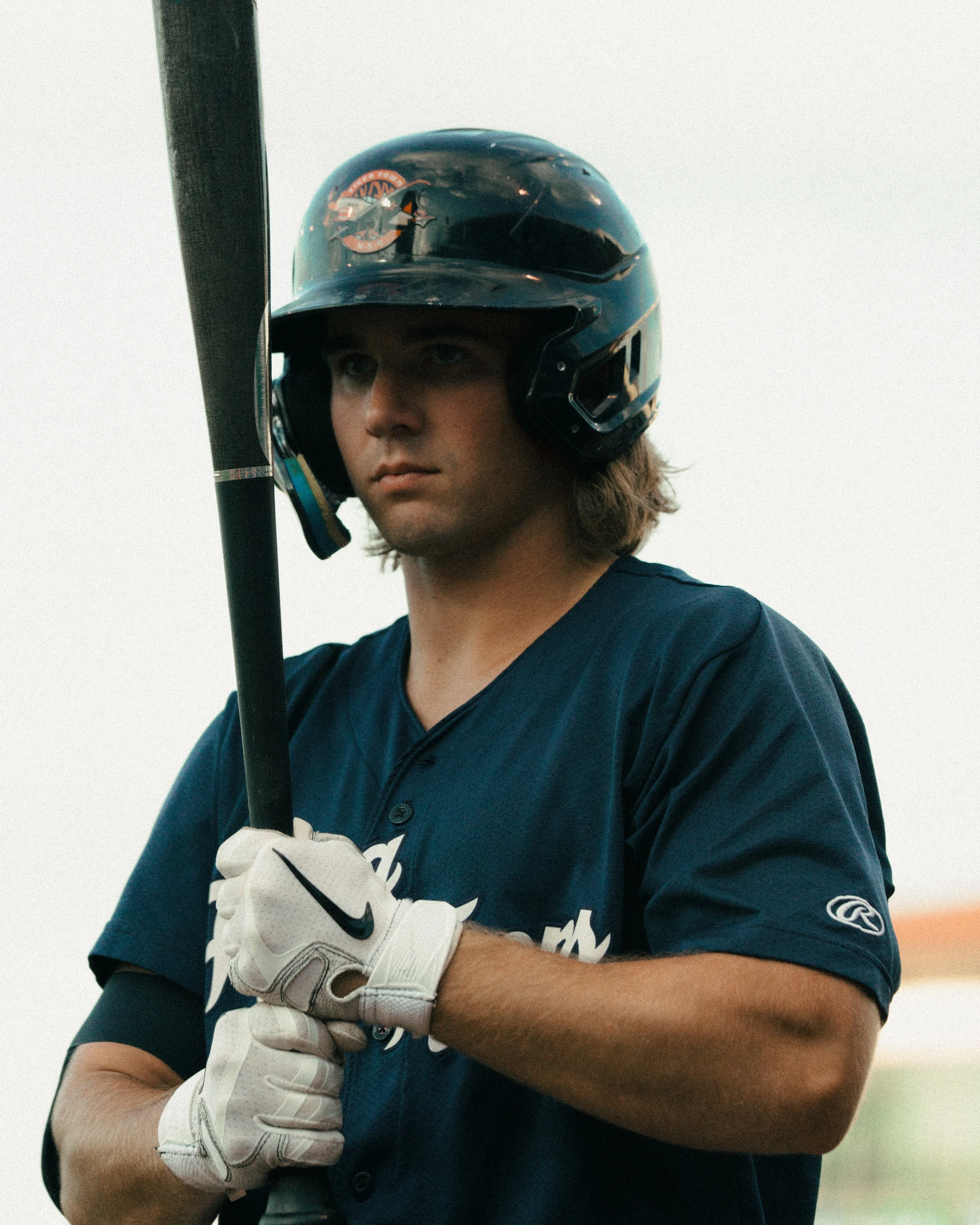 A young baseball player in a blue jersey and a black helmet with a logo, holding a bat with white gloves.