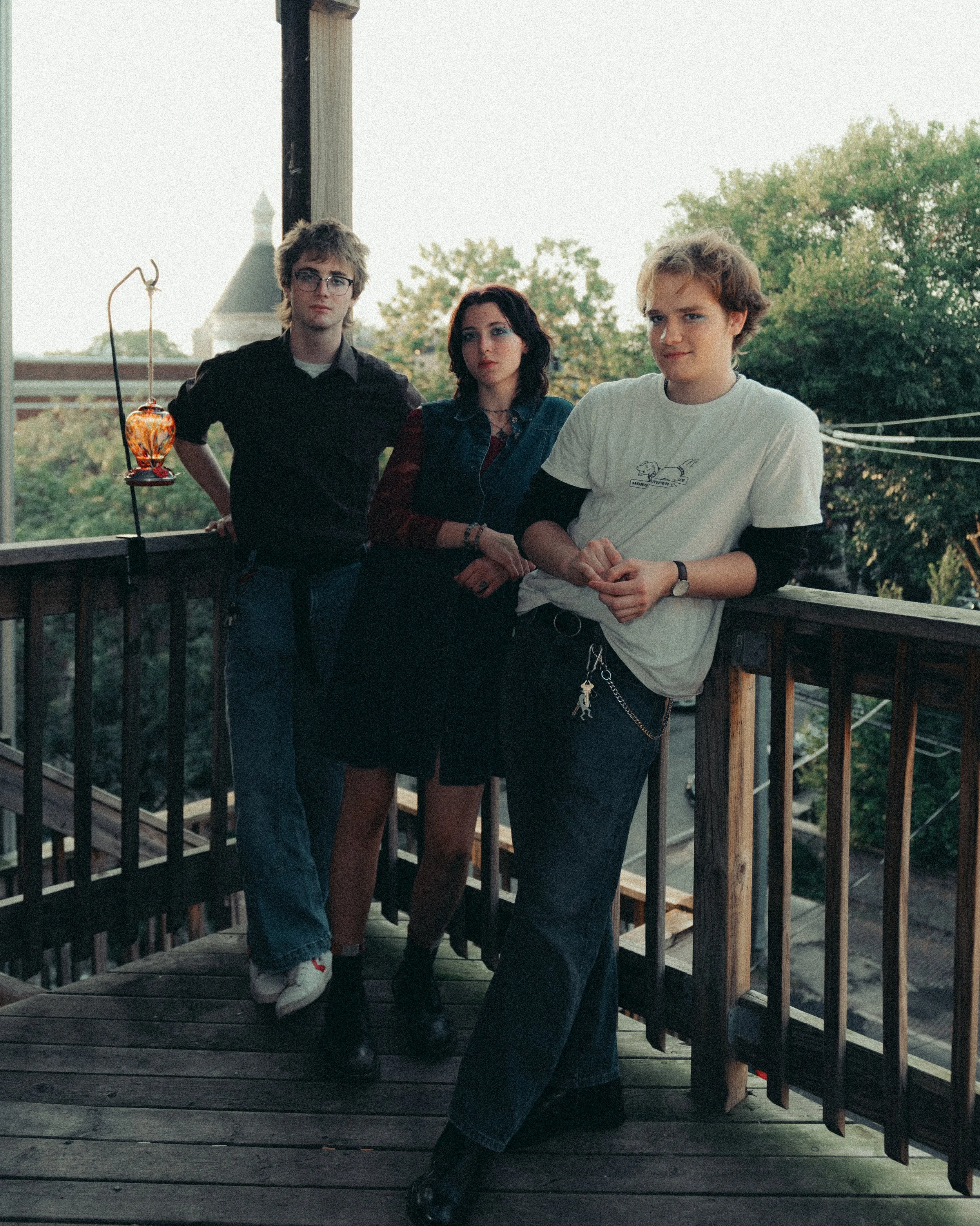 Three young adults standing on a wooden balcony with trees in the background