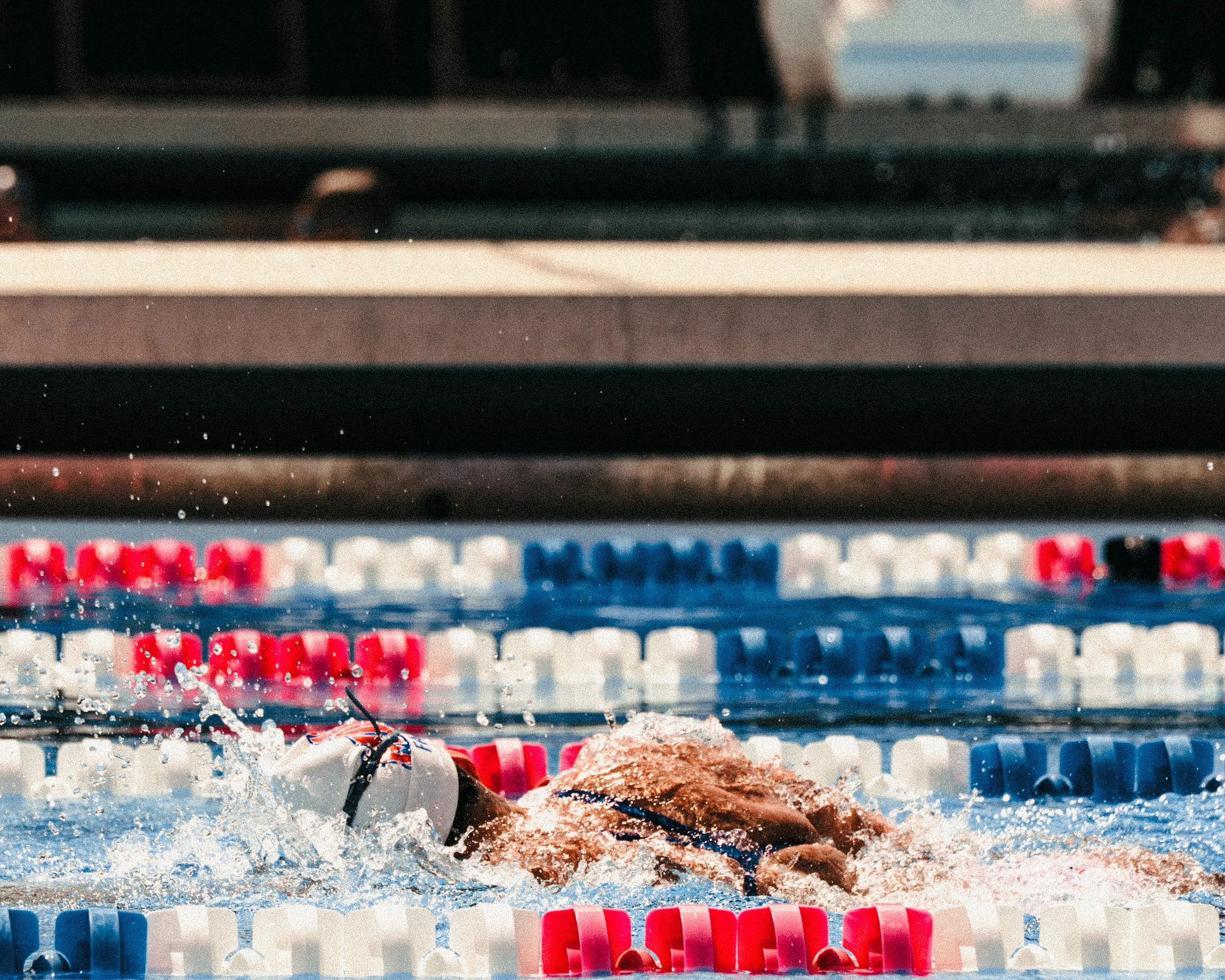 A swimmer performing a freestyle stroke in a swimming pool with lane dividers in white, red, and blue.